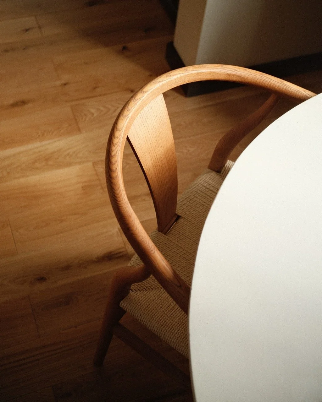 A wooden chair with a curved backrest sitting next to a round white table on a wooden floor.