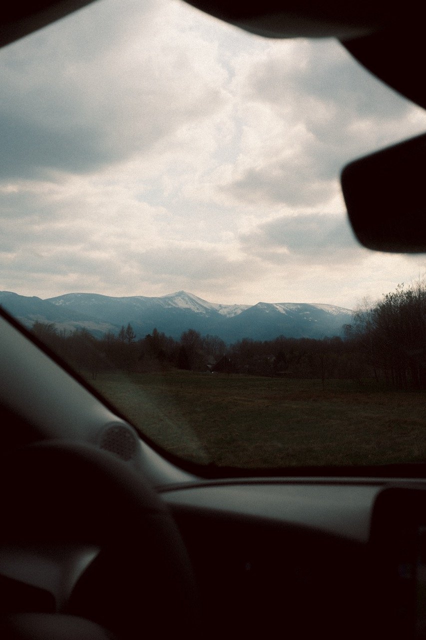 View of snow-capped mountains through a car window on a cloudy day.