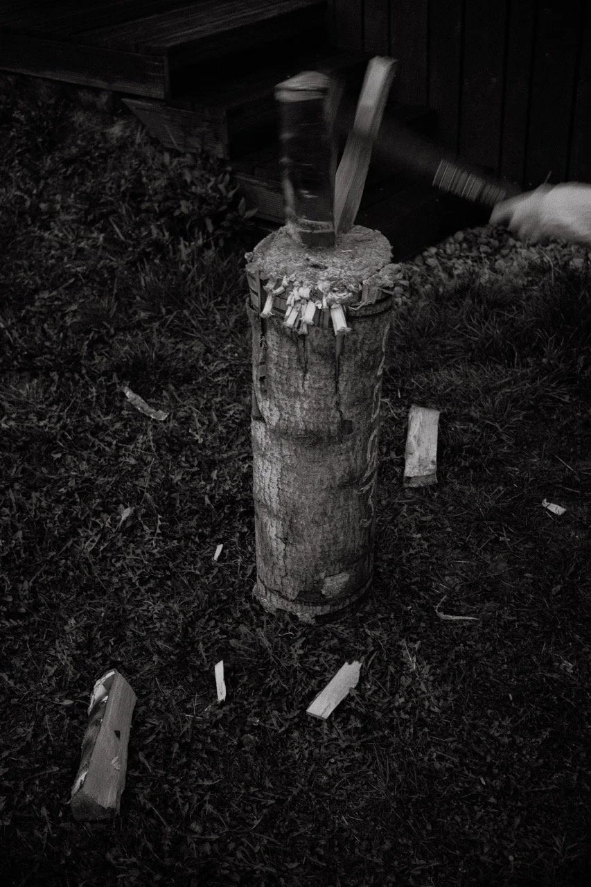 Someone using a hammer to split a log on a tree stump outdoors at night.