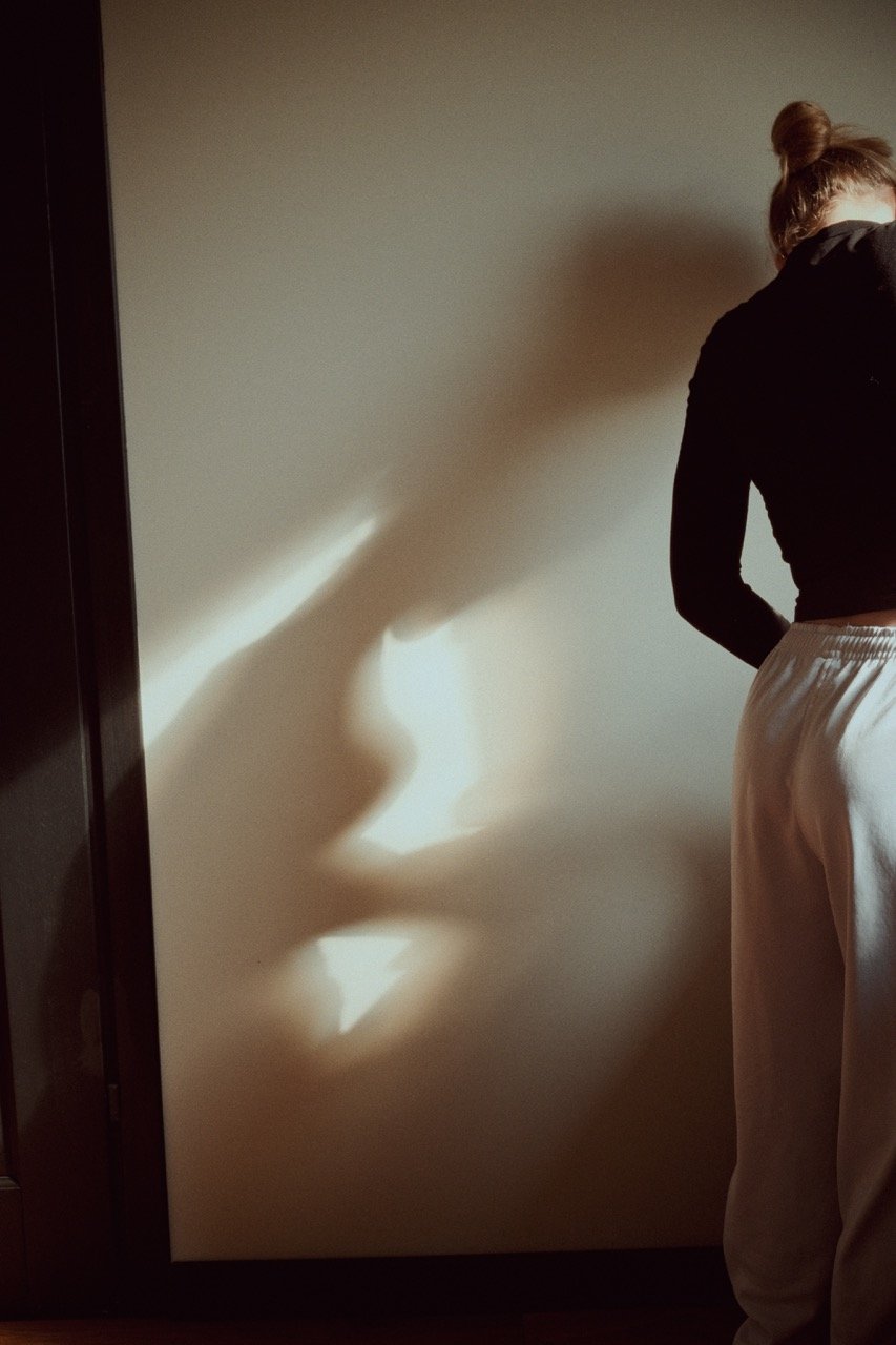 A shadow of a woman's face, profile view, appears on a wall, with a person standing next to it partially visible.