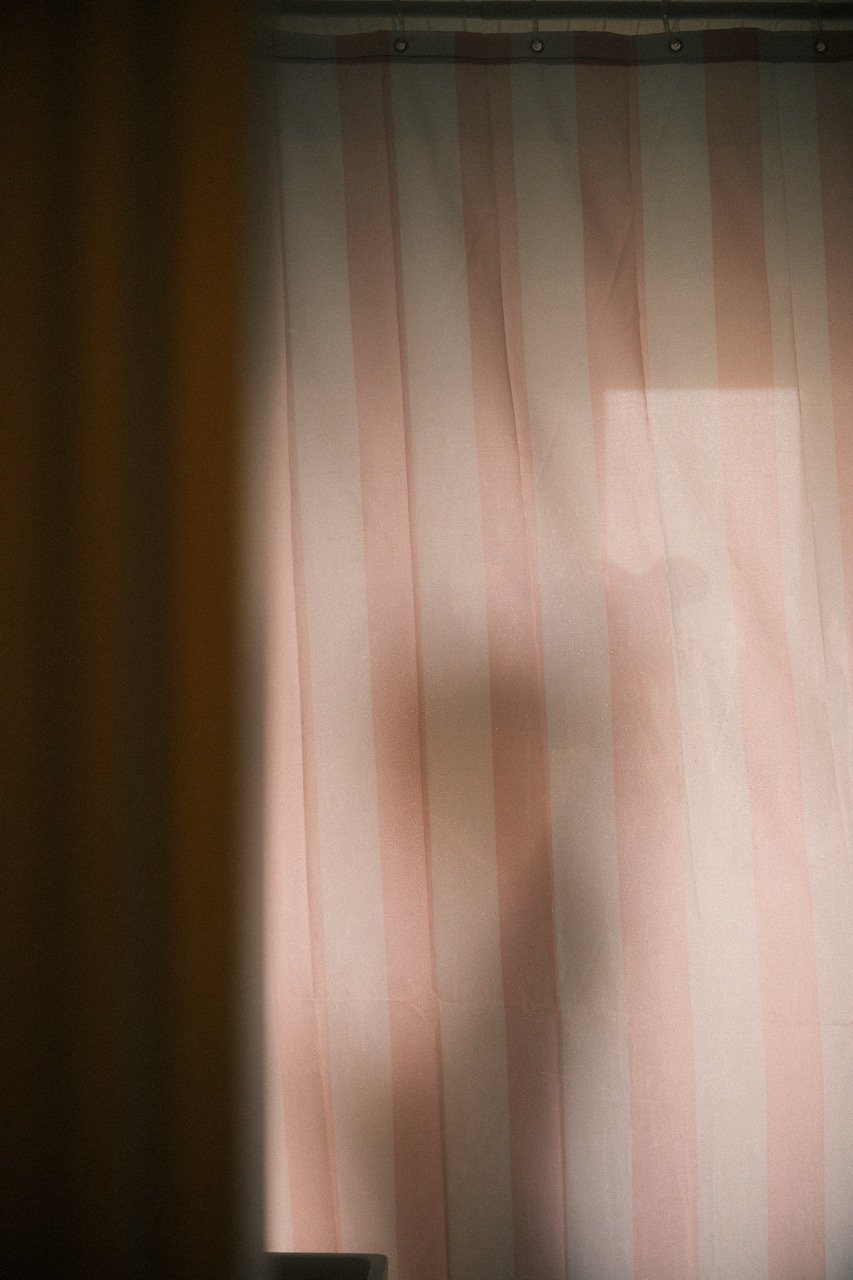 A person taking a mirror selfie in a room with pink vertical striped curtains, with their silhouette visible.