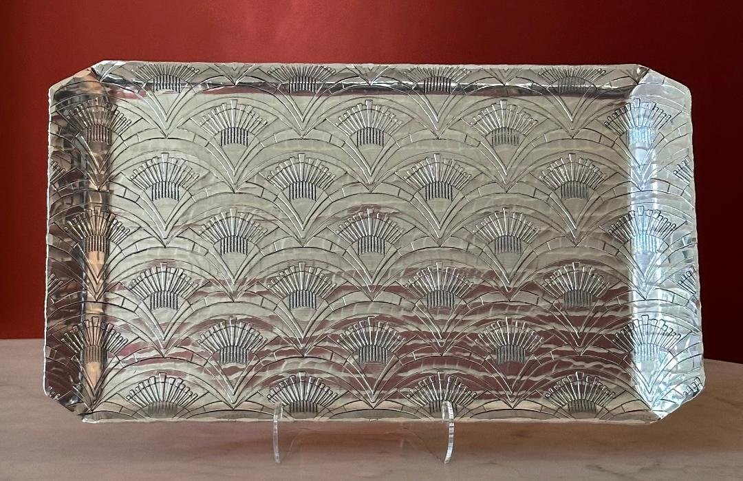 Rectangular decorative silver tray with an Art Deco fan pattern, placed on a wooden surface against a dark red background.