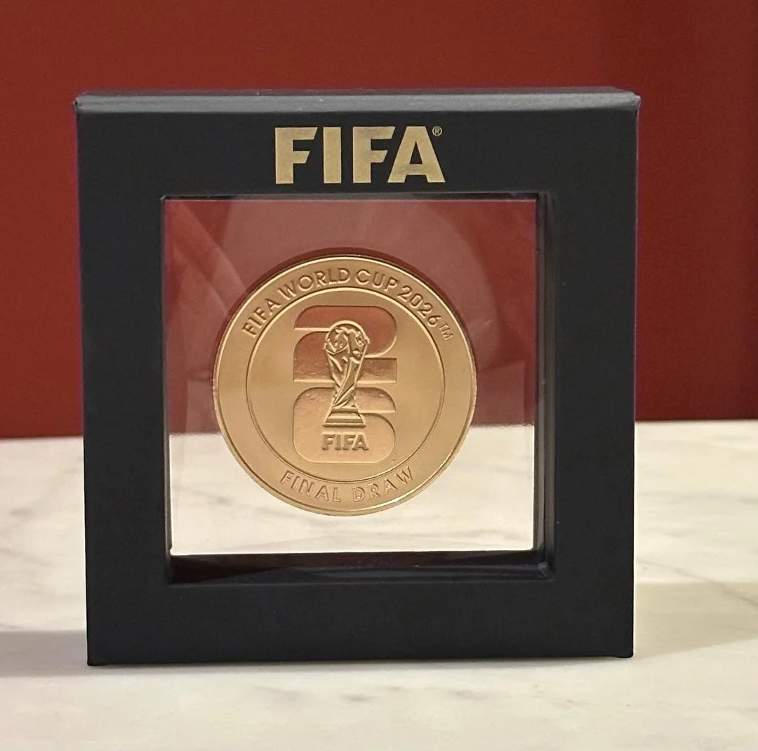 A gold-colored commemorative coin inside a black frame with a clear front, featuring the FIFA logo and text about the 2022 FIFA World Cup final.