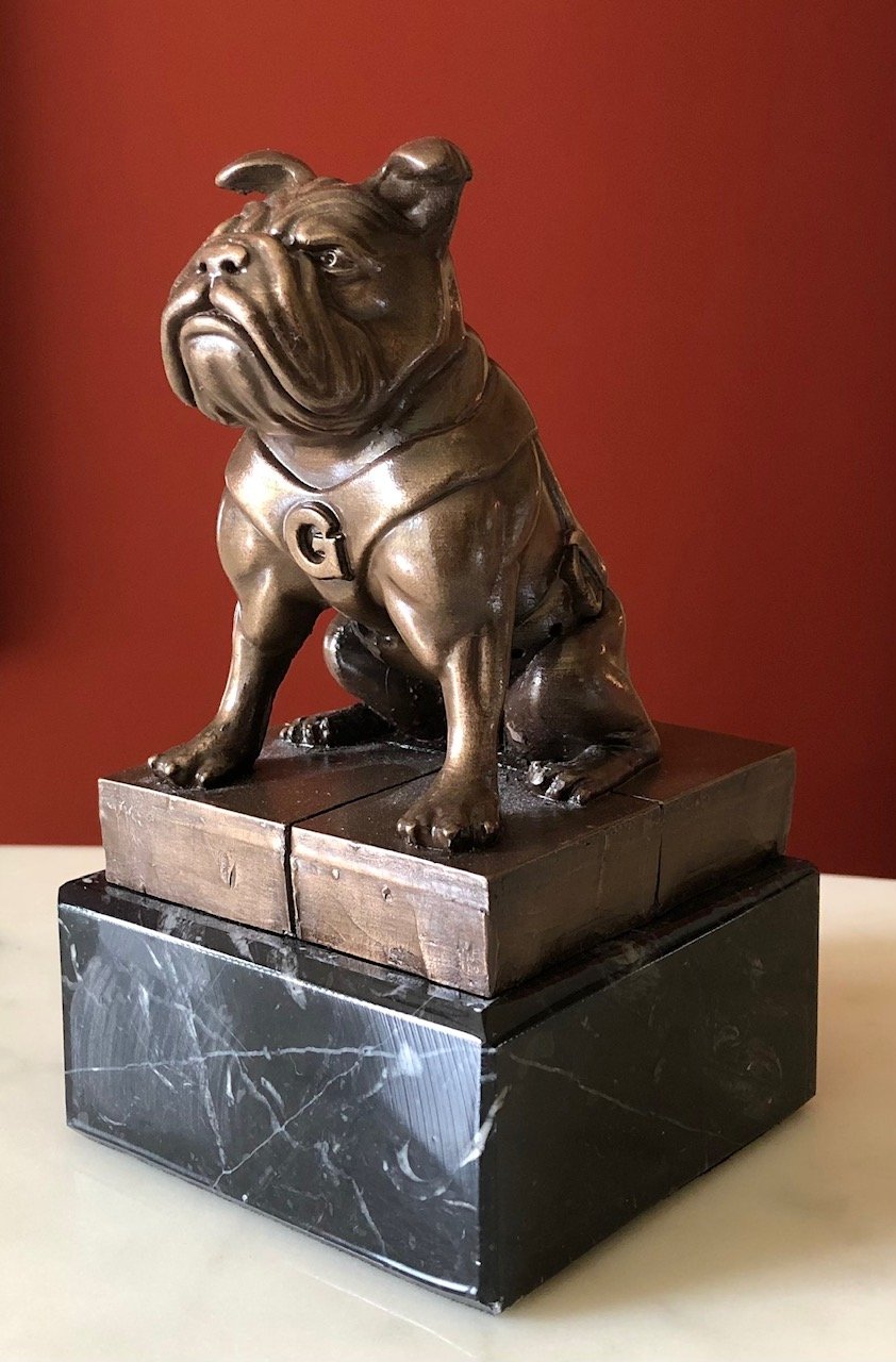 Bronze sculpture of a sitting bulldog on a black marble base with a red wall background.