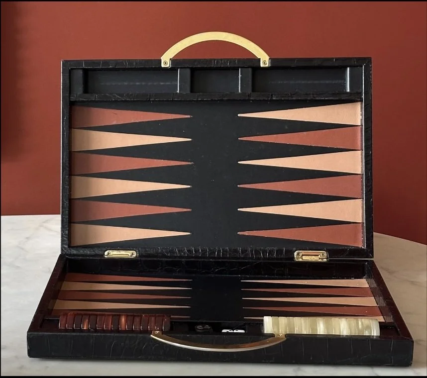 Open custom Italian backgammon game case with playing pieces inside on a marble surface, against a red wall
