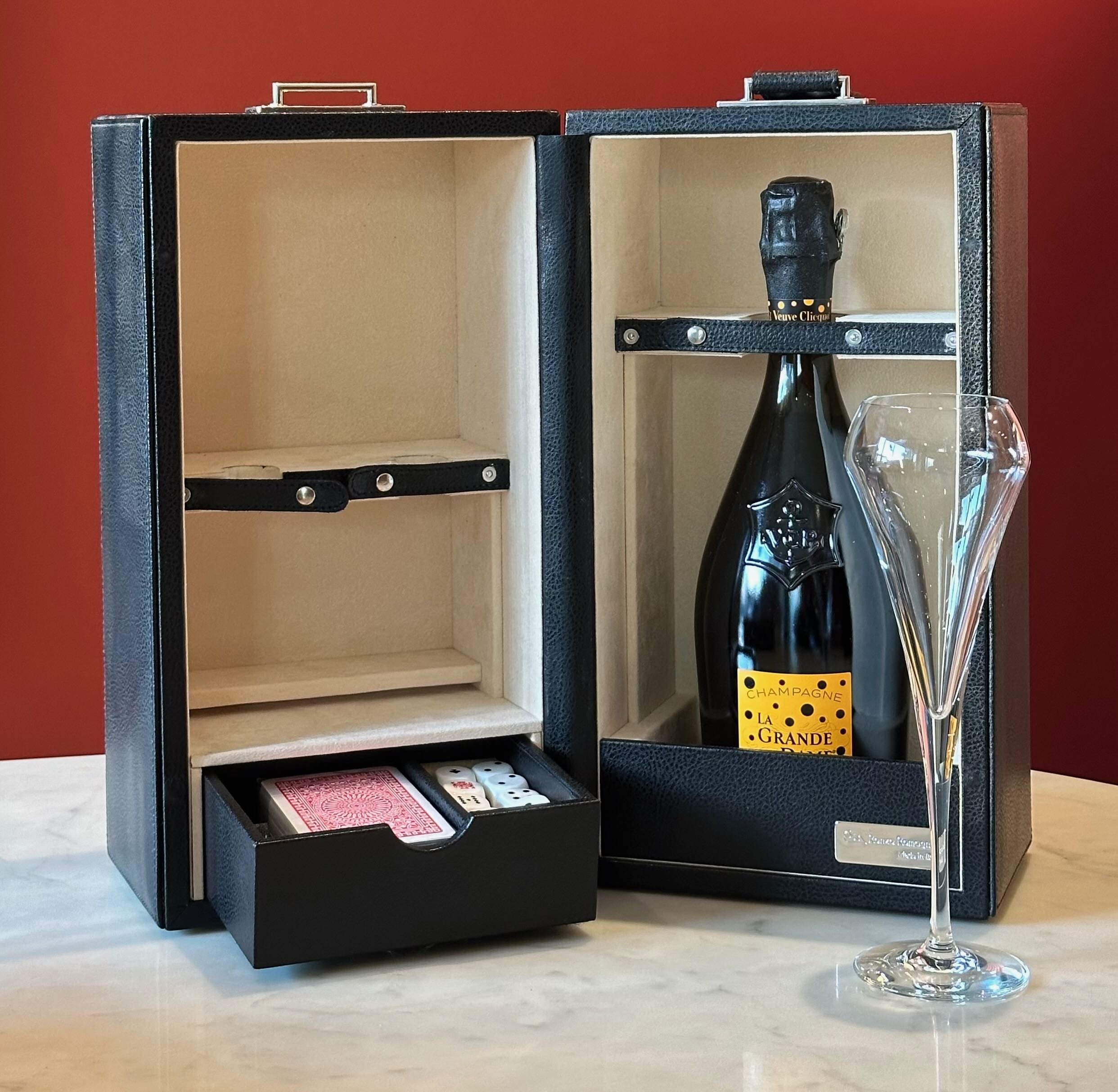 A custom luxury Italian leather champagne box with a bottle of Veuve Clicquot and a champagne flute in front of it, on a white marble surface with a red background for ultra high-networth gifting.