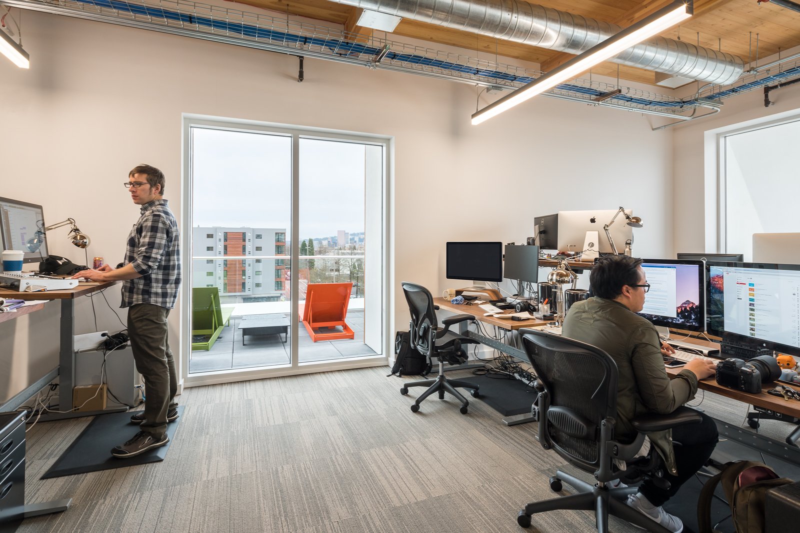 An office with two men working at desks and a balcony with outdoor seating.