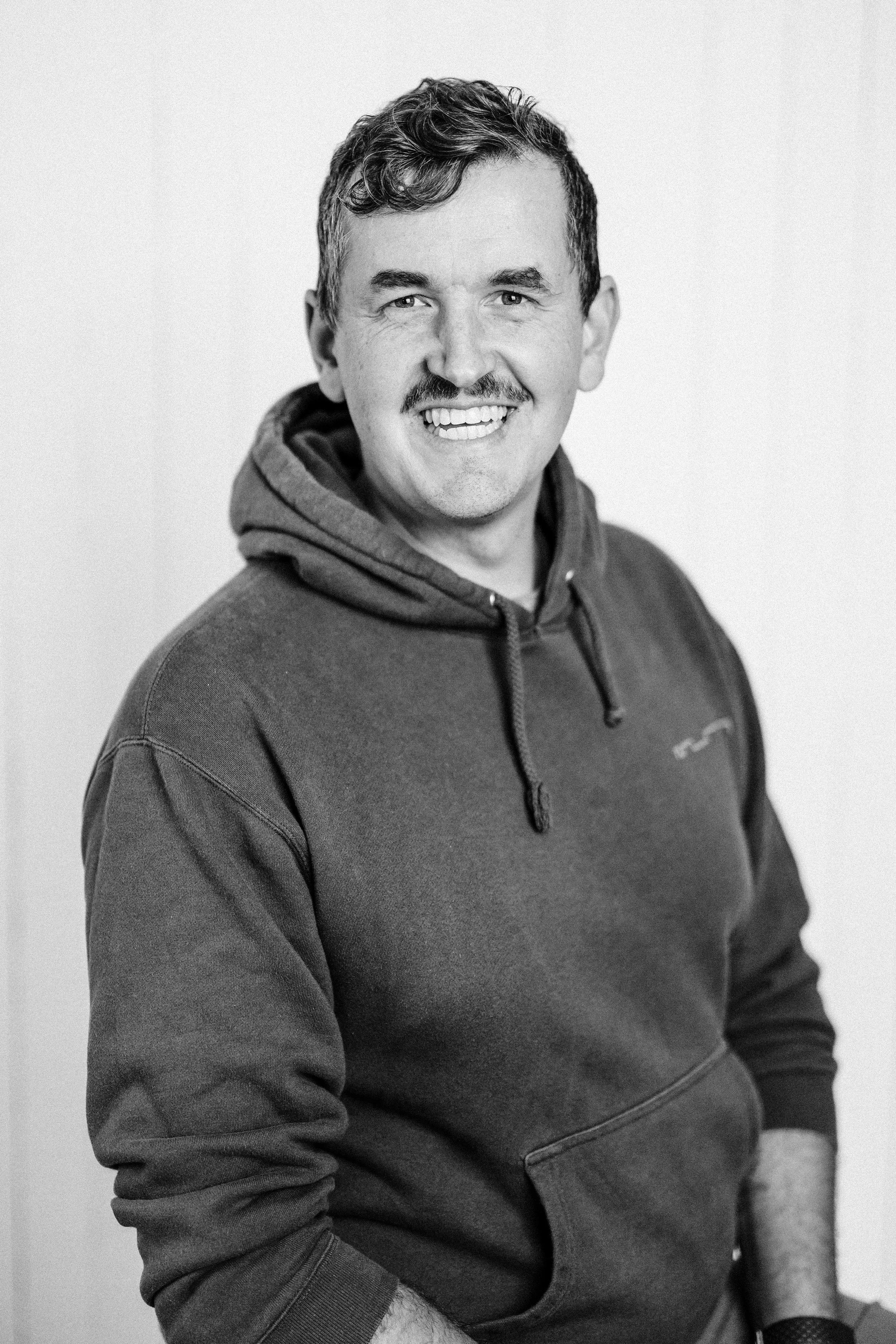 Black and white photo of a smiling person wearing a beanie and plaid shirt.