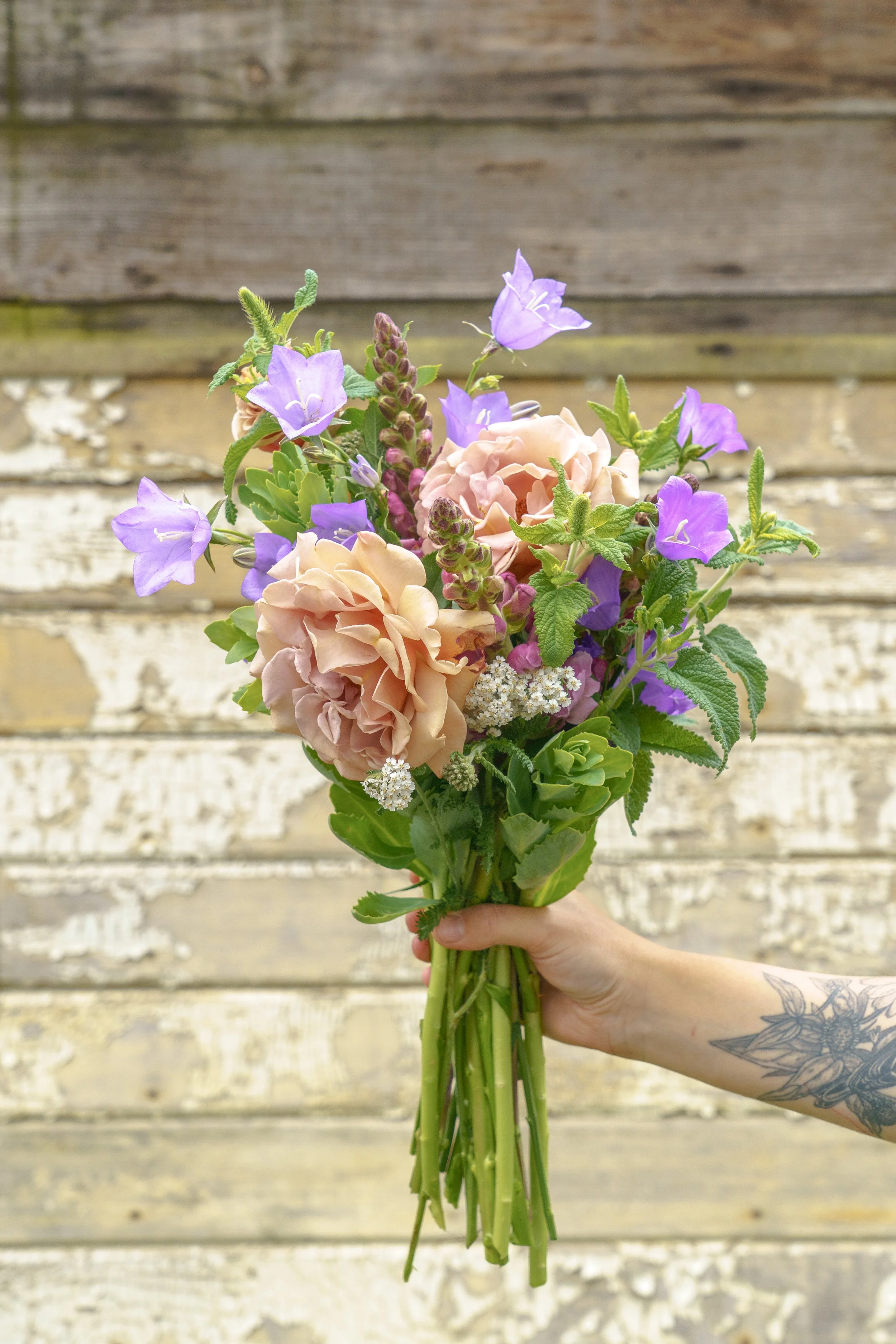 A hand holding a colorful bouquet of flowers with a rustic wooden background.