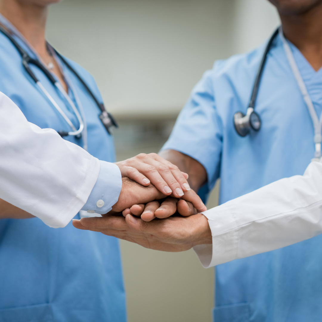 Healthcare professionals in scrubs and stethoscopes stacking hands together.