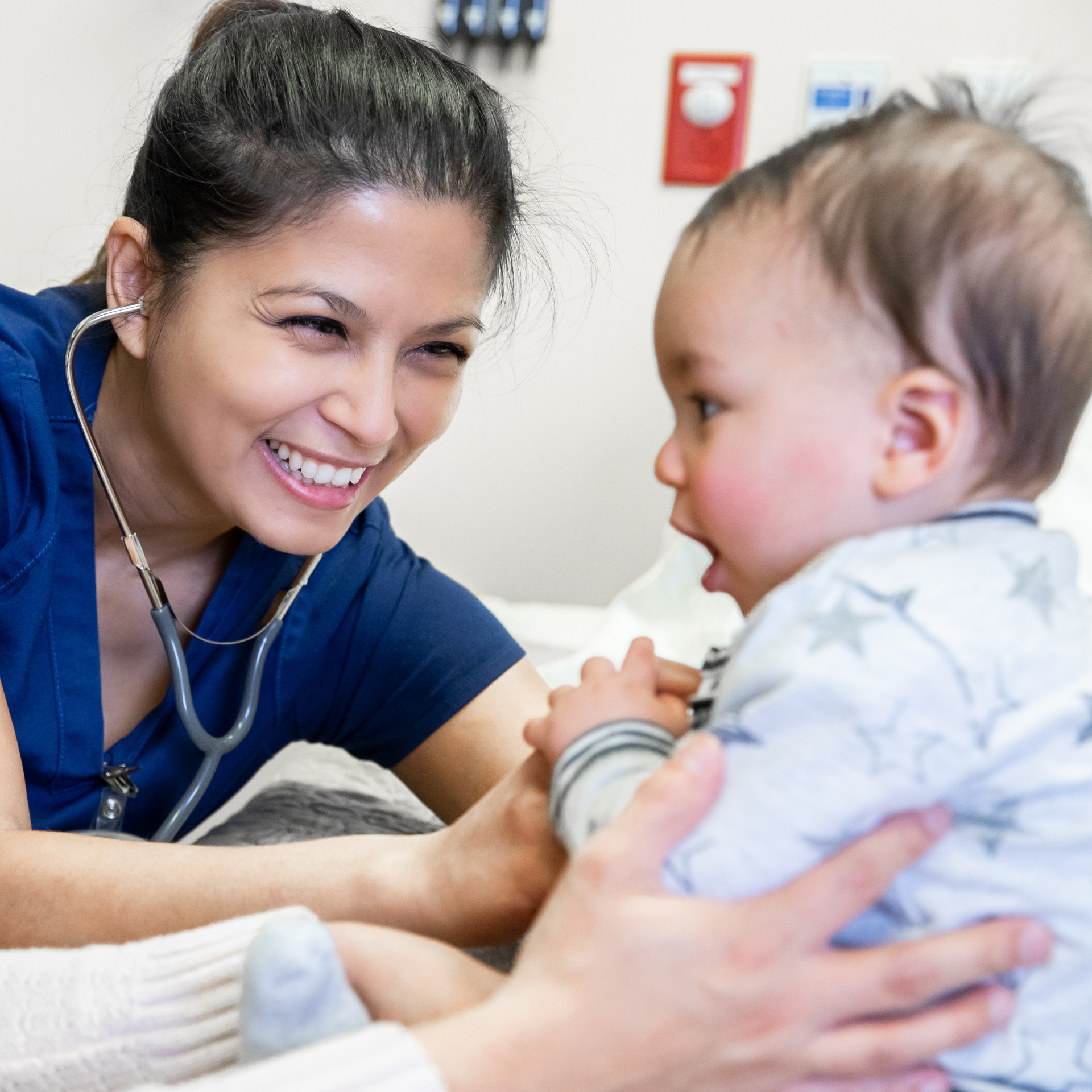 A smiling female healthcare worker with a stethoscope interacting with a young boy in a medical setting.