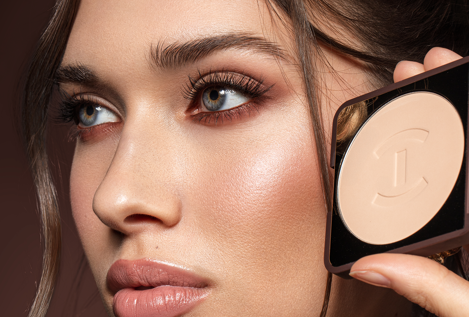 Model holding TRU(HUE) foundation, emphasizing cosmetic product packaging, complexion makeup design, and premium brand presentation.