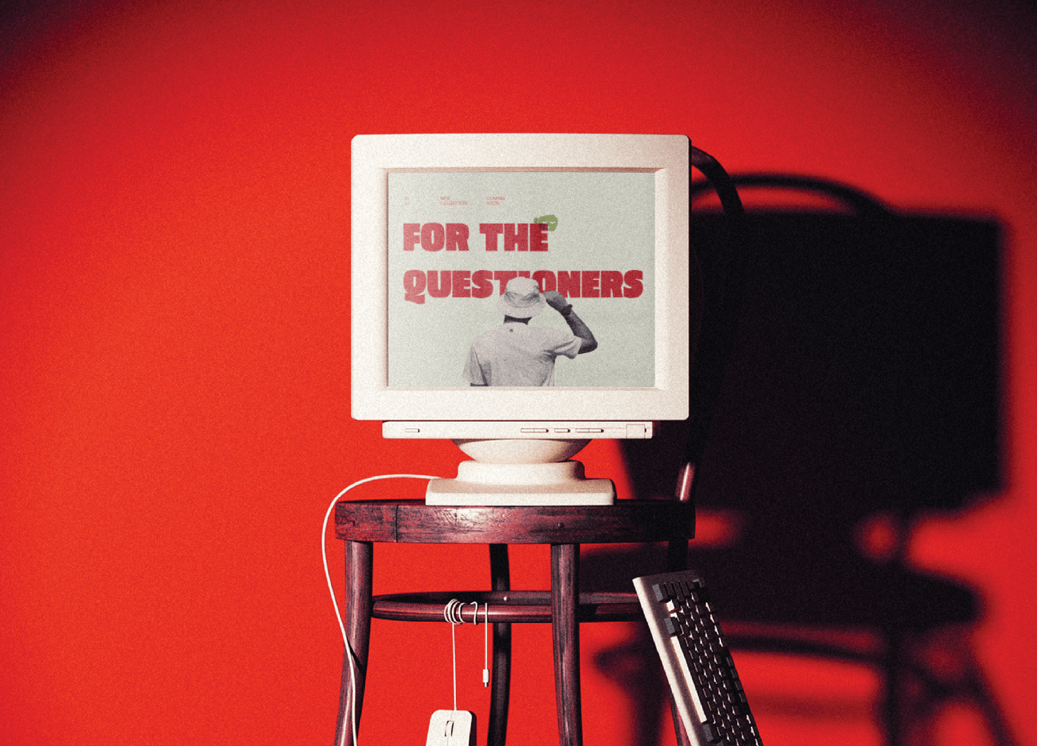 Vintage computer on wooden stool with screen displaying 'For the Questioners' against red background.
