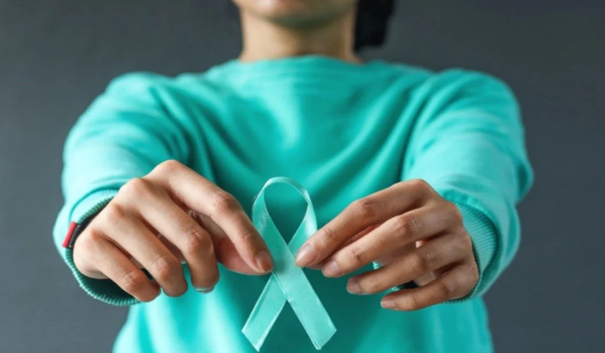 Person wearing teal shirt holding out a teal ribbon, the symbol for sexual assault awareness