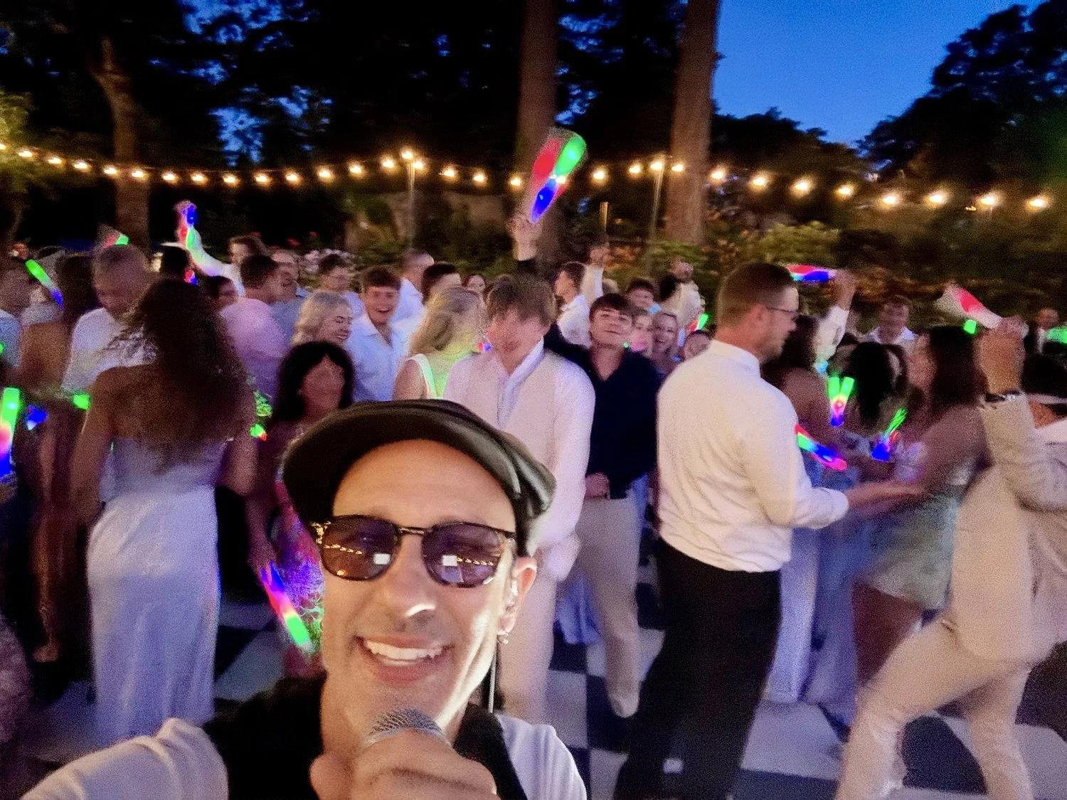 Hit Machine's performer with fans enjoying an evening outdoor show under string lights