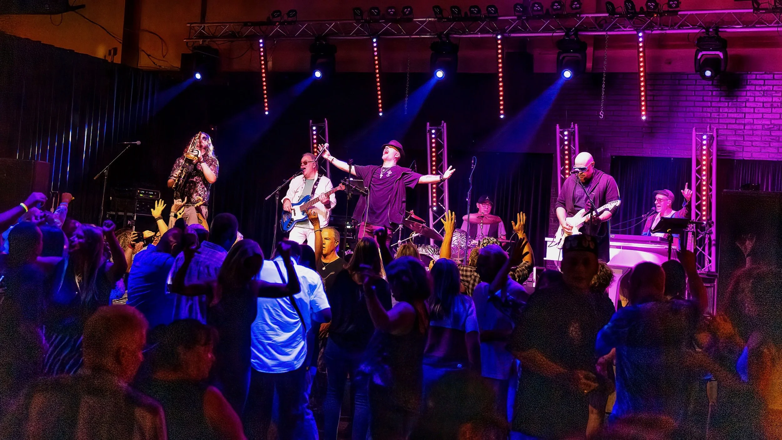 Man wearing a hat and leather jacket, smiling, with lights blurred in the background.