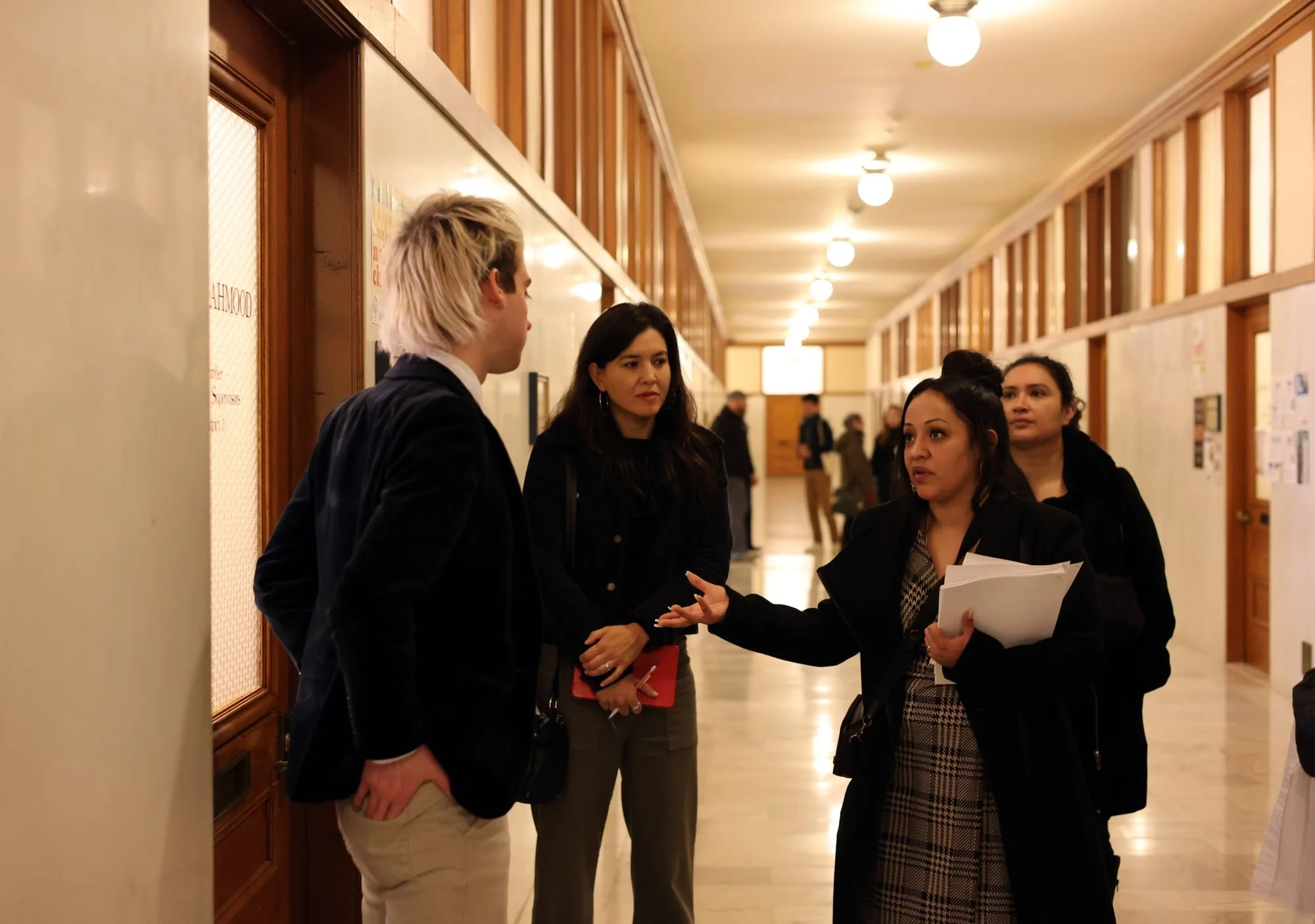 three women standing in the hallway of san francisco city hall talking to a legislative aide