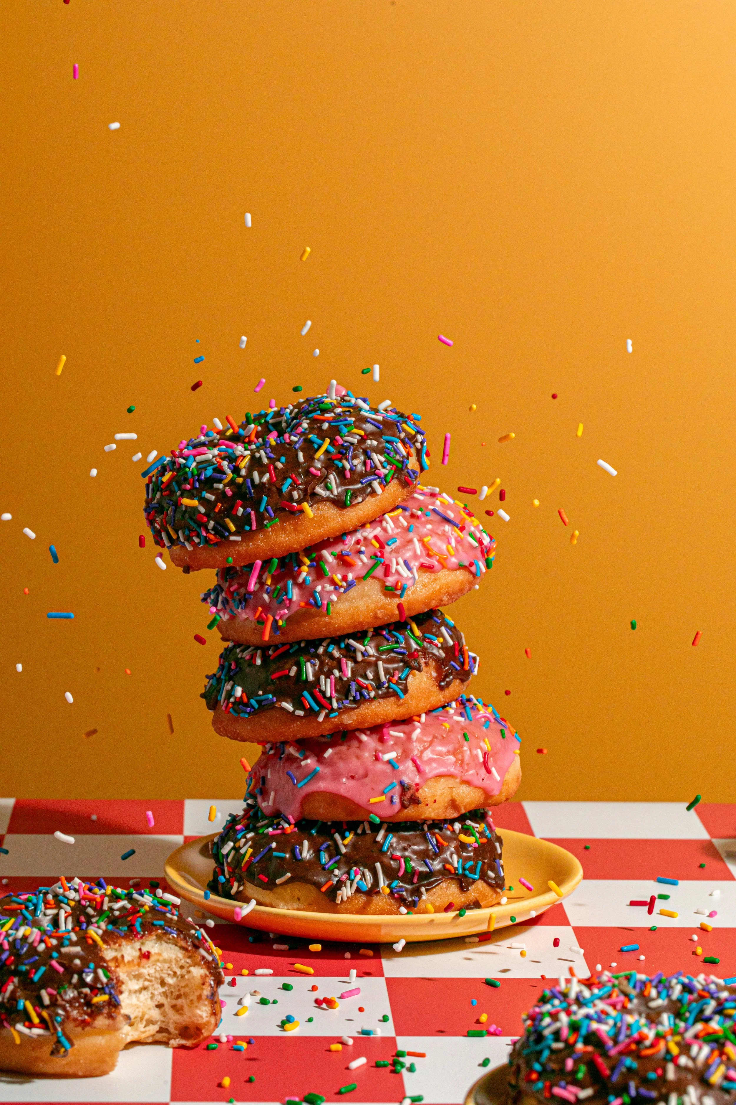 pile of tipsy chocolate pink sprinkle donuts on a yellow background seattle food and breakfast photographer