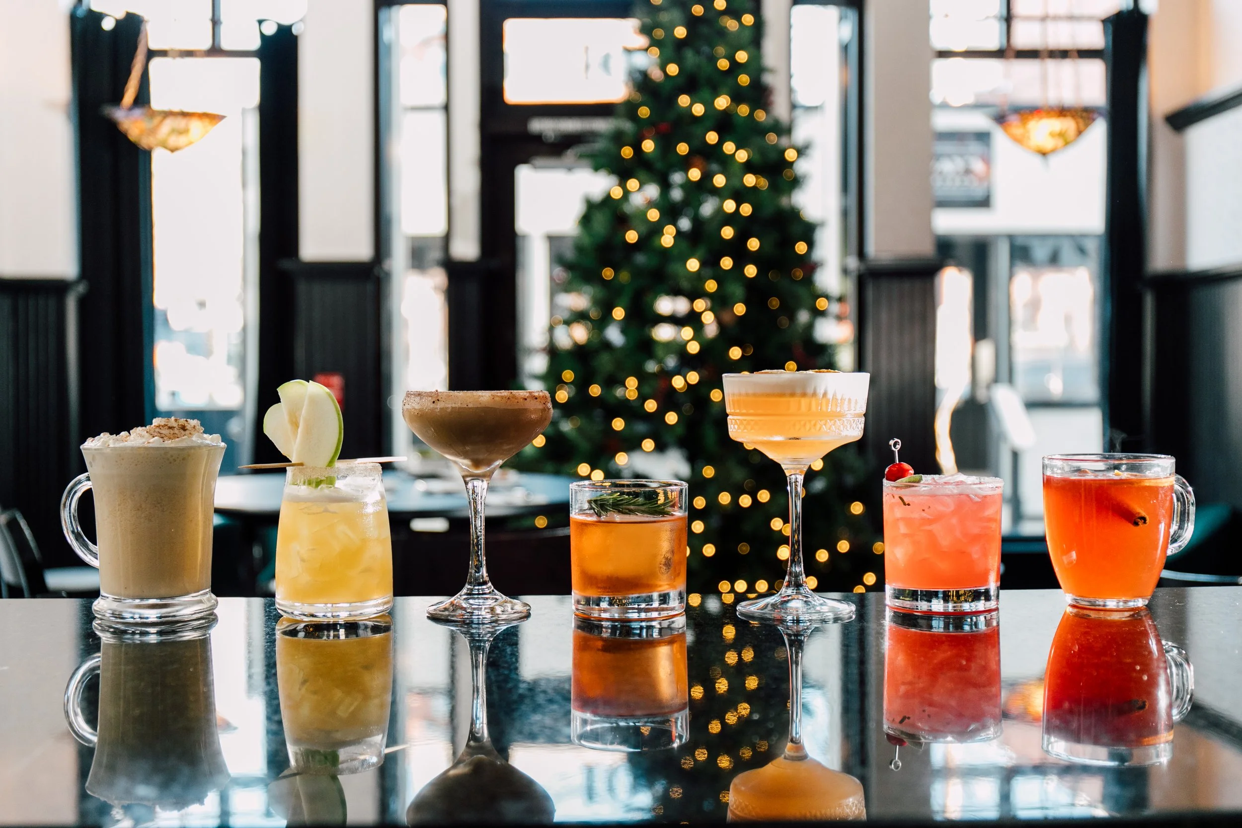 holiday cocktail lineup with twinkling christmas tree behind the bar hospitality photography