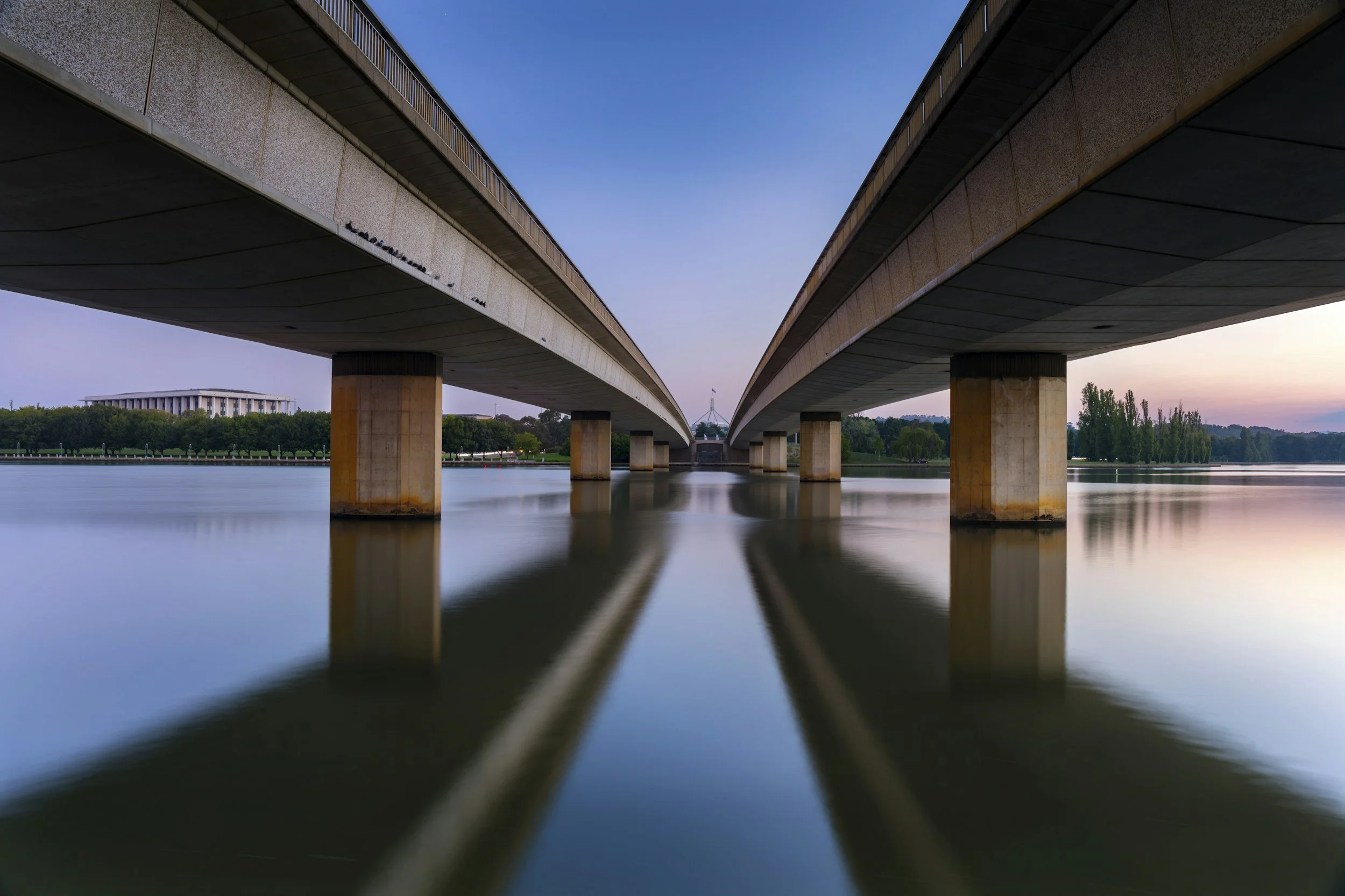 View of Lake Burley Griffin Canberra with the bridge overhead symbolising the need for marketing for trades in Canberra. The photo is taken from below the bridge, showing the reflection of the bridge's supports in the water.