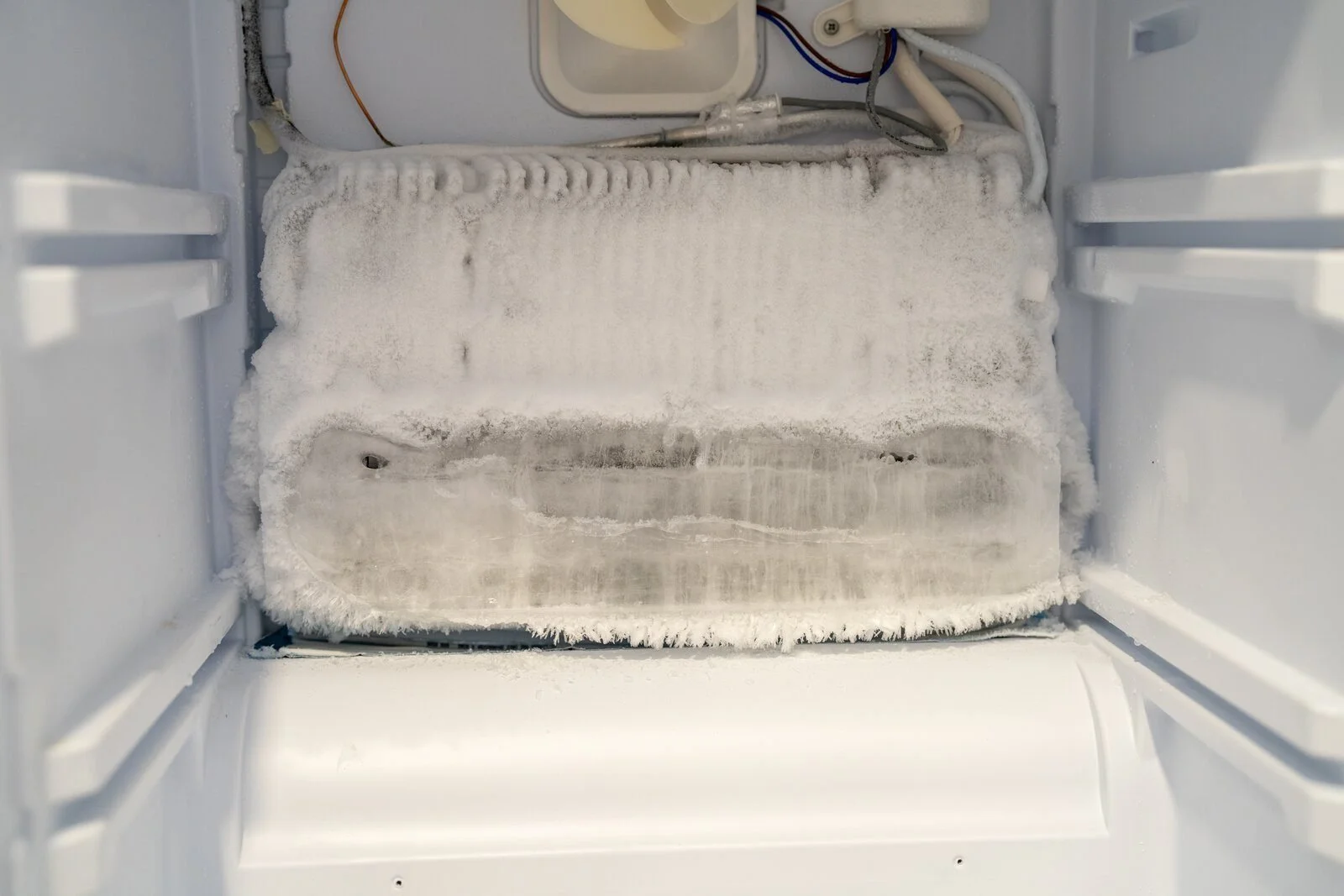 Freezer with the back panel removed, showing the evaporator coil encased in frost from a failed defrost system