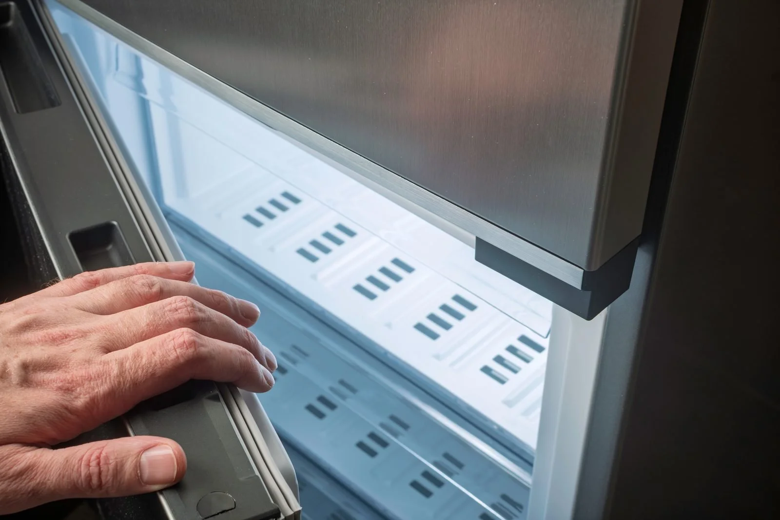 Hand pressing on the rubber door gasket of an open stainless steel refrigerator to check the door seal
