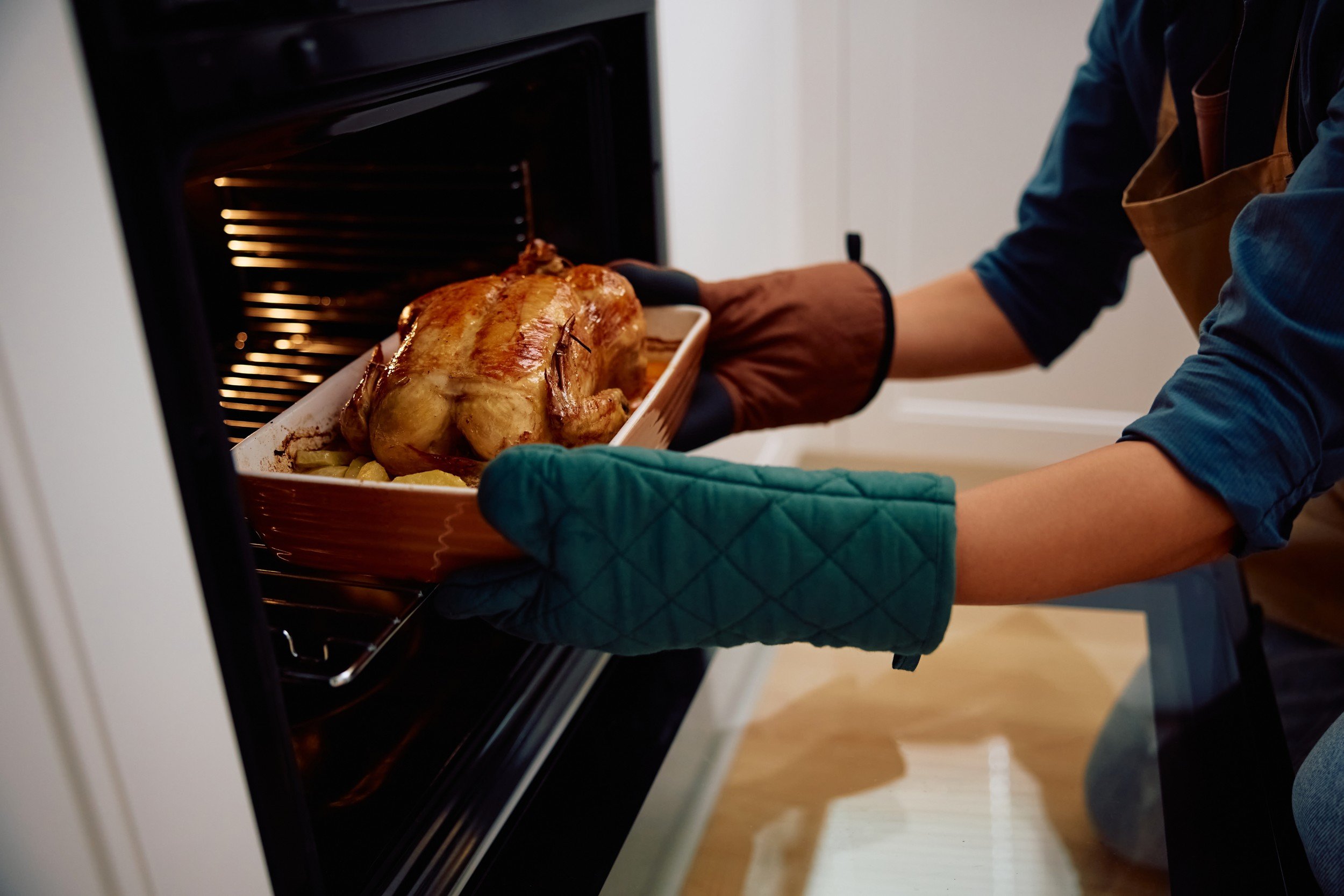 Roasted holiday bird being taken out of a hot oven with oven mitts