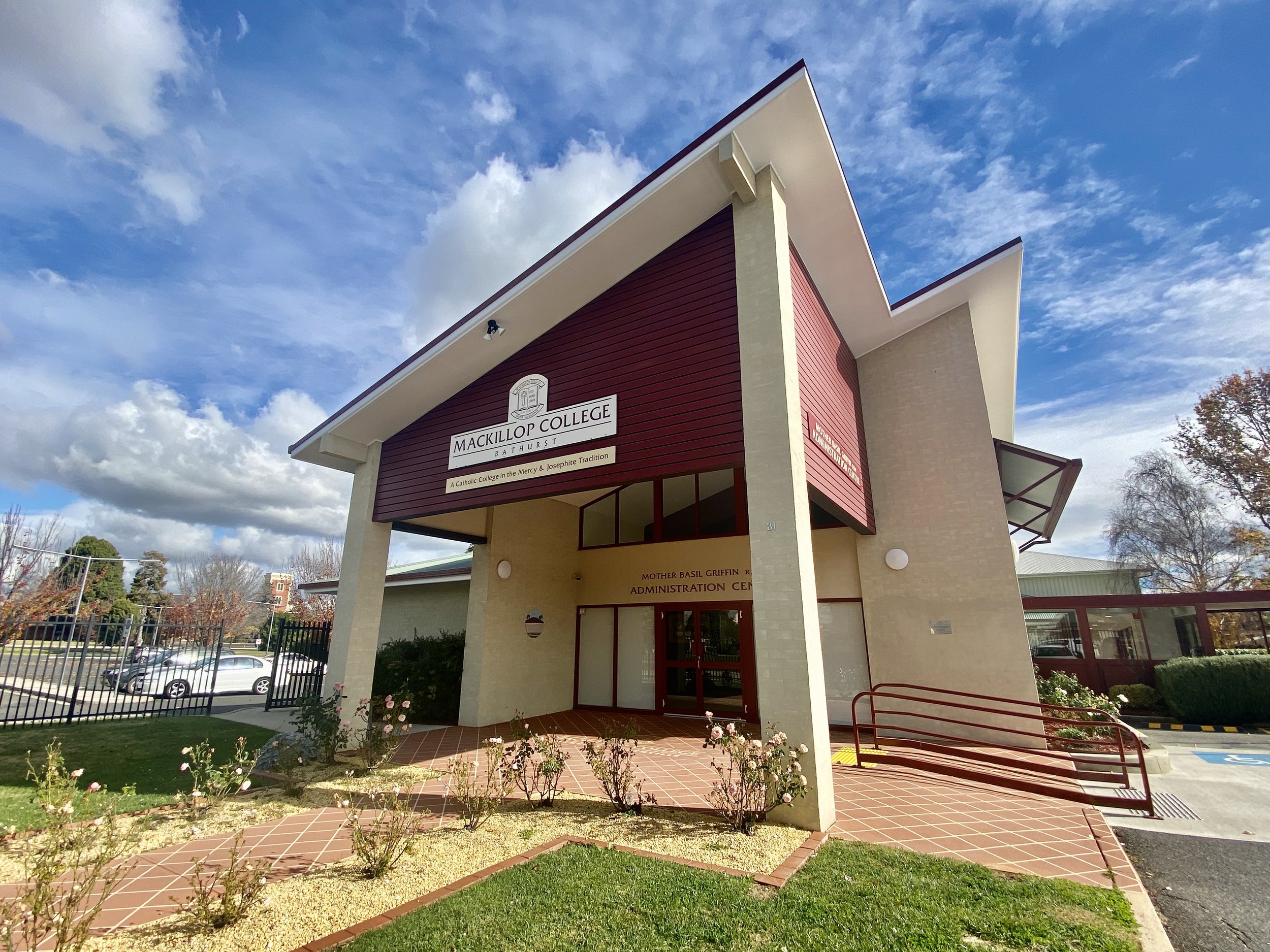Mackillop College Bathurst entrance with modern architectural design and landscaped garden, under a blue sky with clouds.