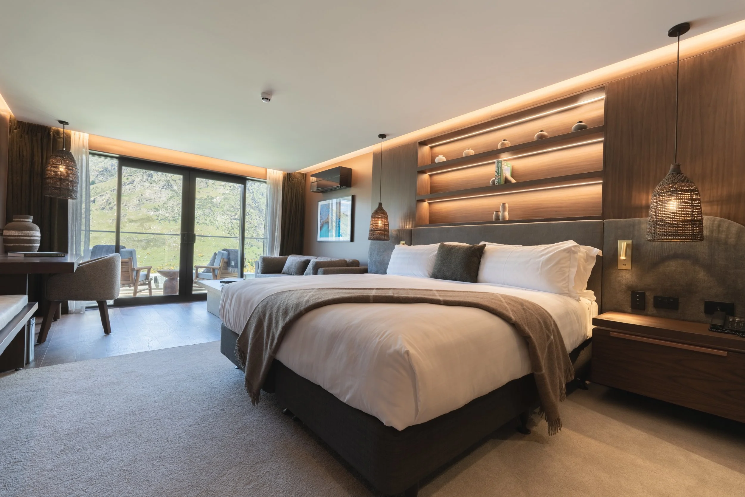 Luxury hotel bedroom with super-king bed, warm timber shelving and ambient lighting at Coronet Ridge Resort Queenstown.