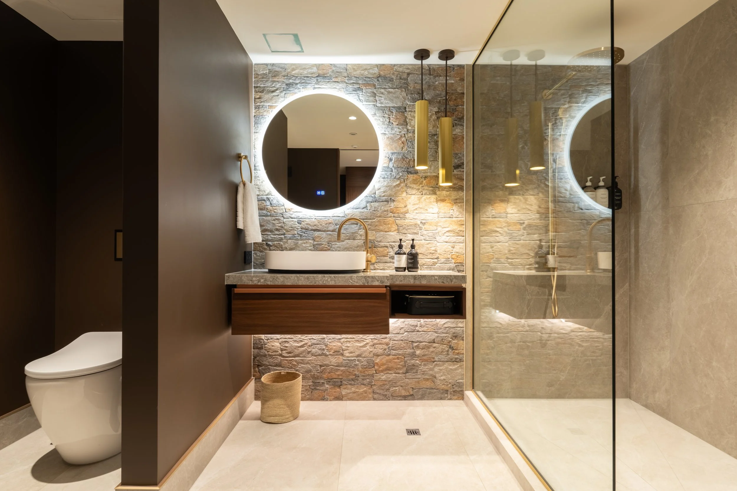 Modern bathroom with stone finishes, timber vanity and round illuminated mirrors