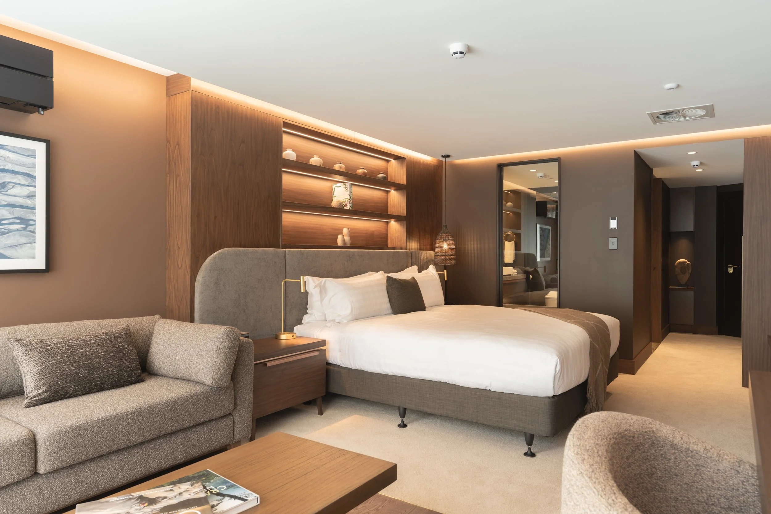 Luxury bedroom with super-king bed, timber shelving and warm ambient lighting.