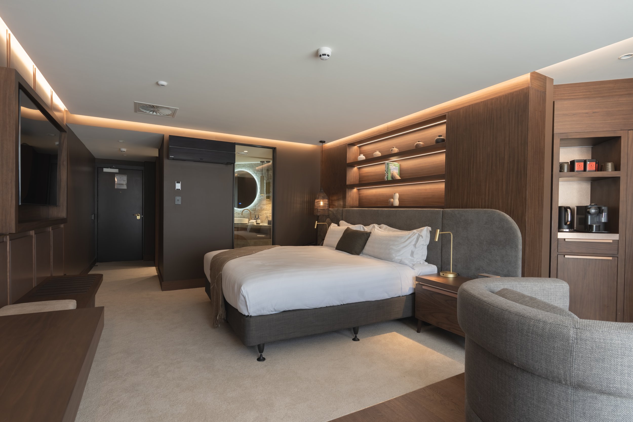 Luxury hotel bedroom with super-king bed, timber shelving and warm ambient lighting.
