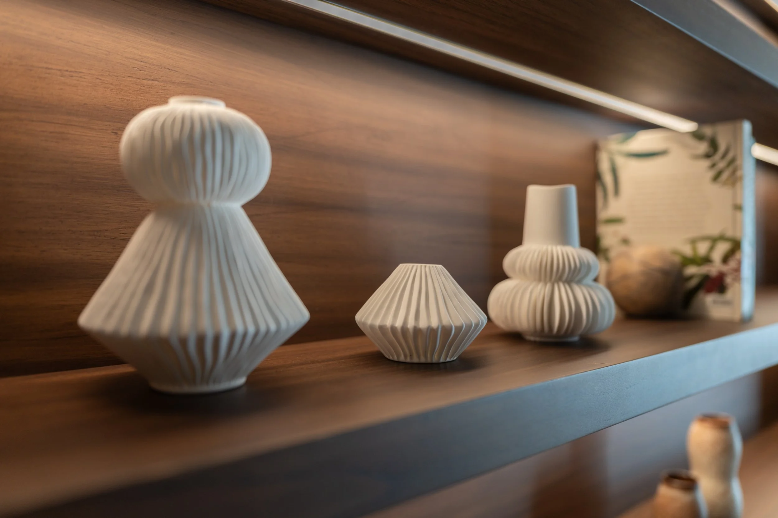 Decorative vases displayed on timber shelf with soft accent lighting.