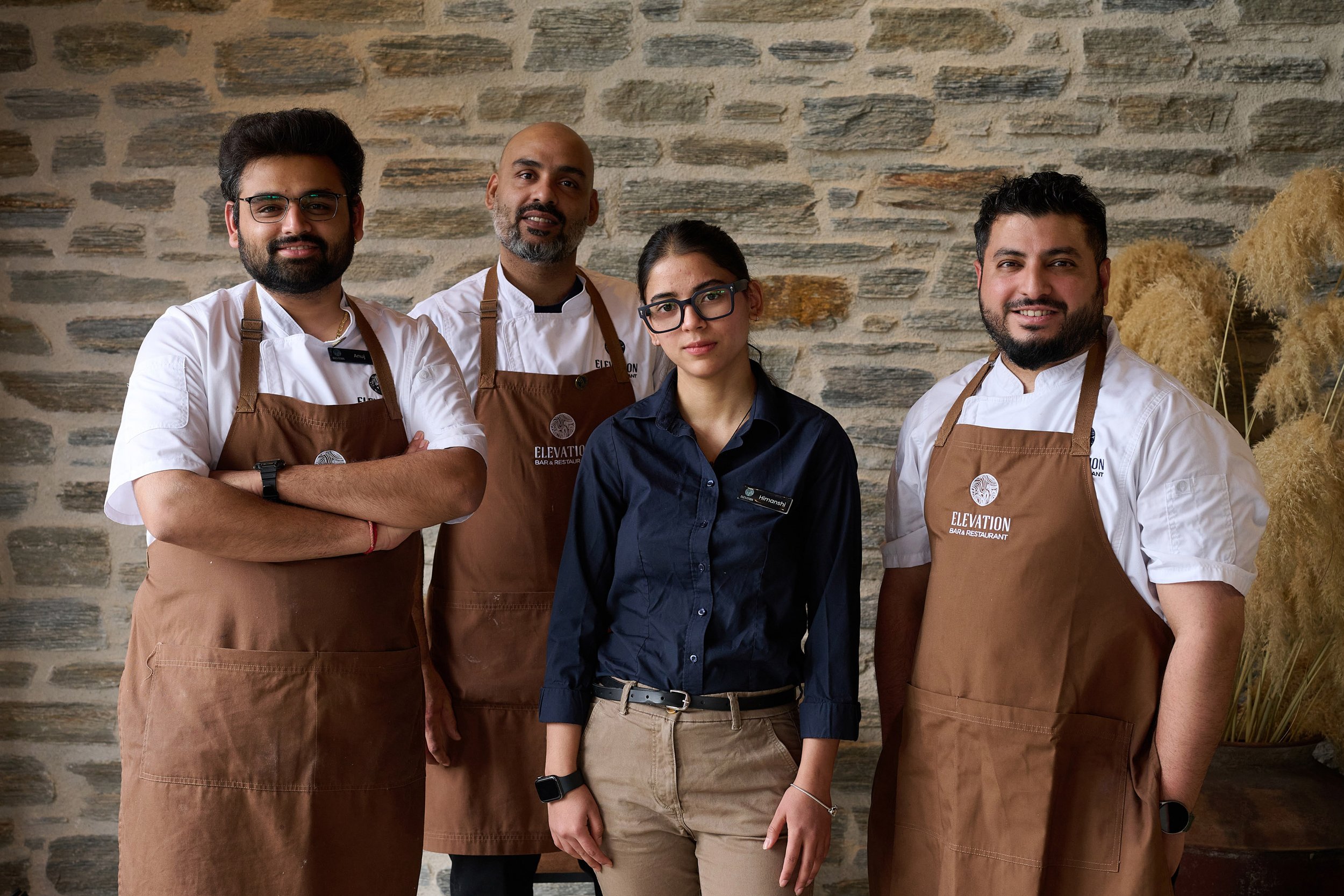 Team at Elevation Bar & Restaurant Queenstown in uniform standing in front of stone wall.