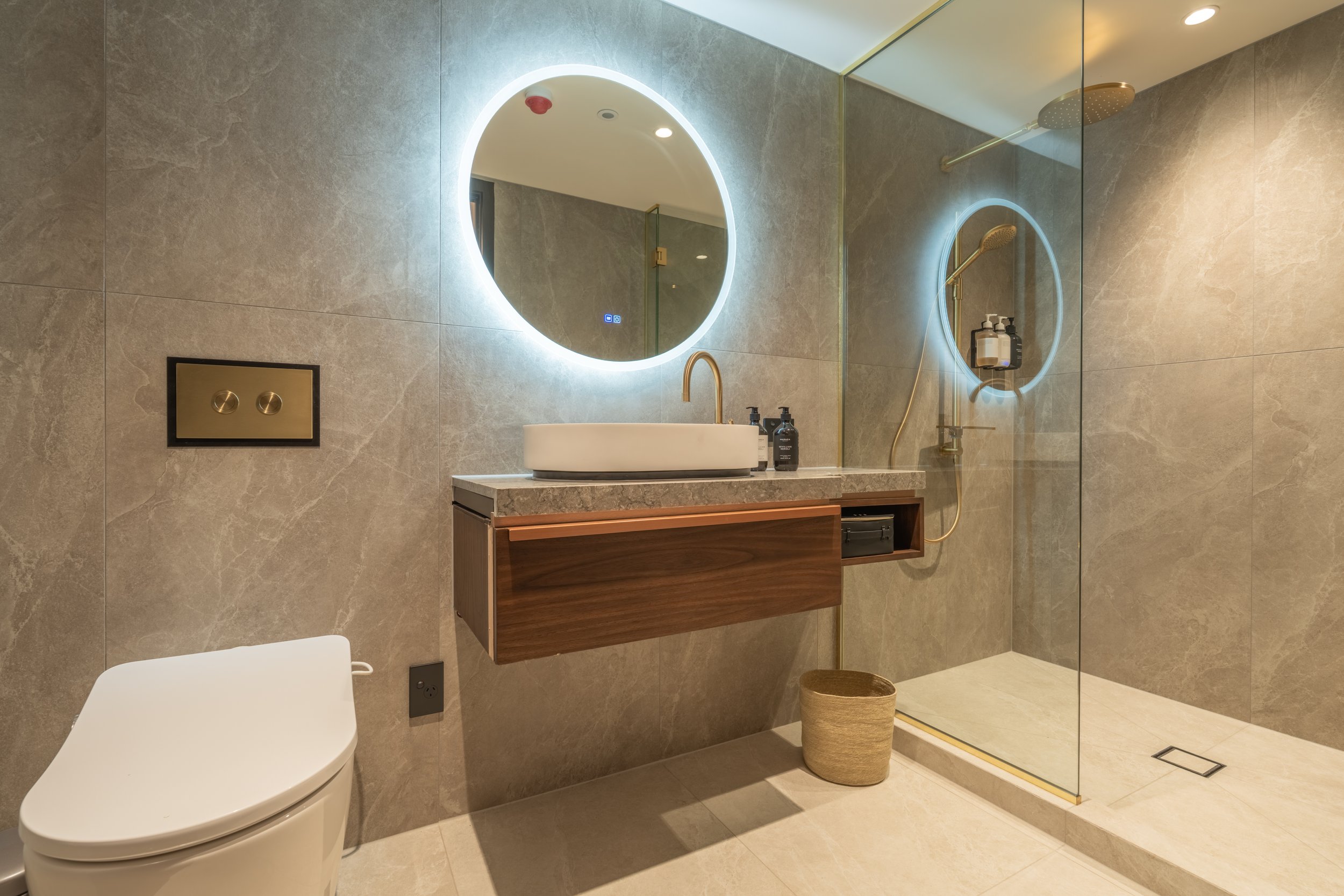 Luxury bathroom vanity with round illuminated mirror, stone tiles and timber cabinetry at Coronet Ridge Resort.