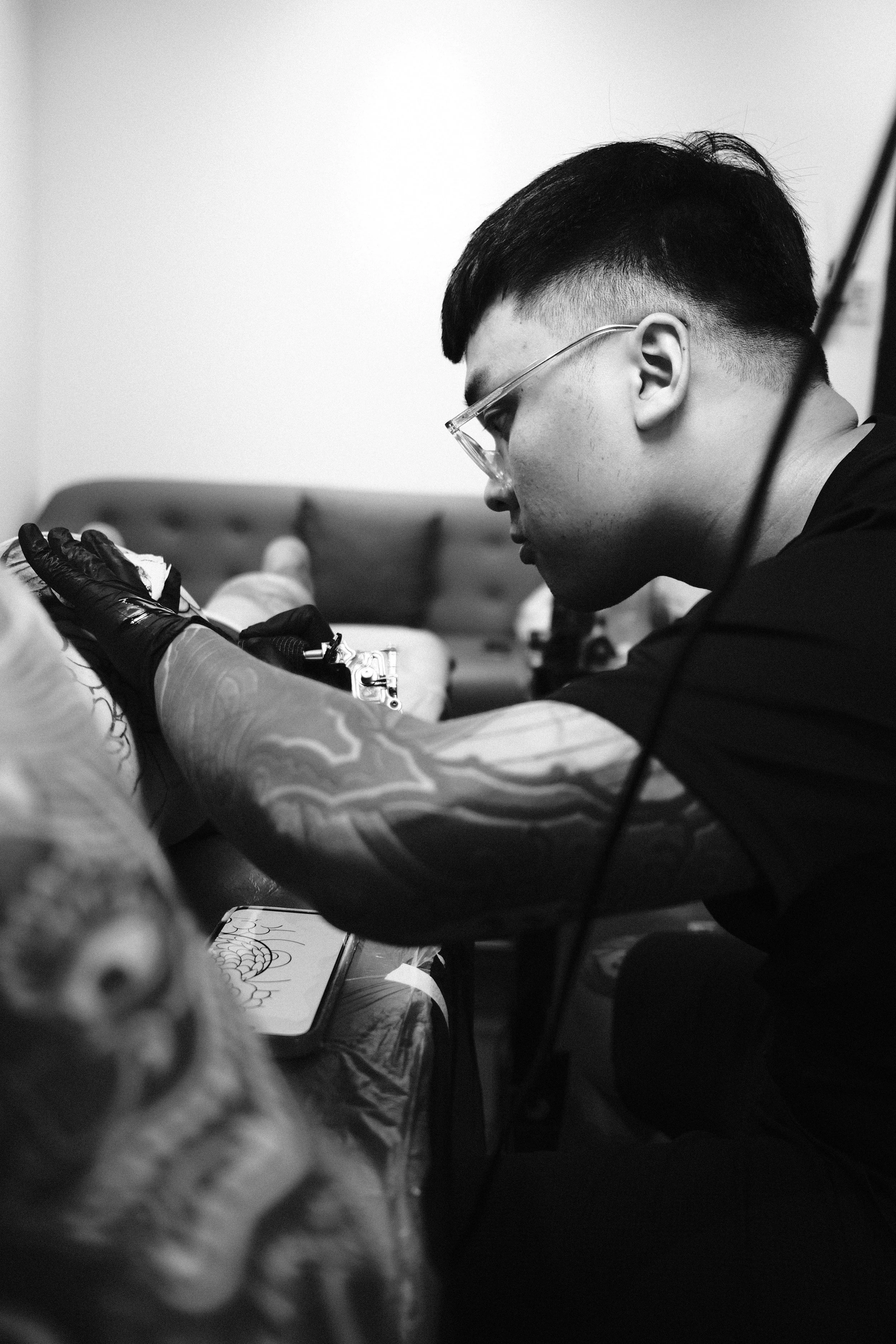 Tattoo artist with glasses and tattoo sleeve working on a client's tattoo