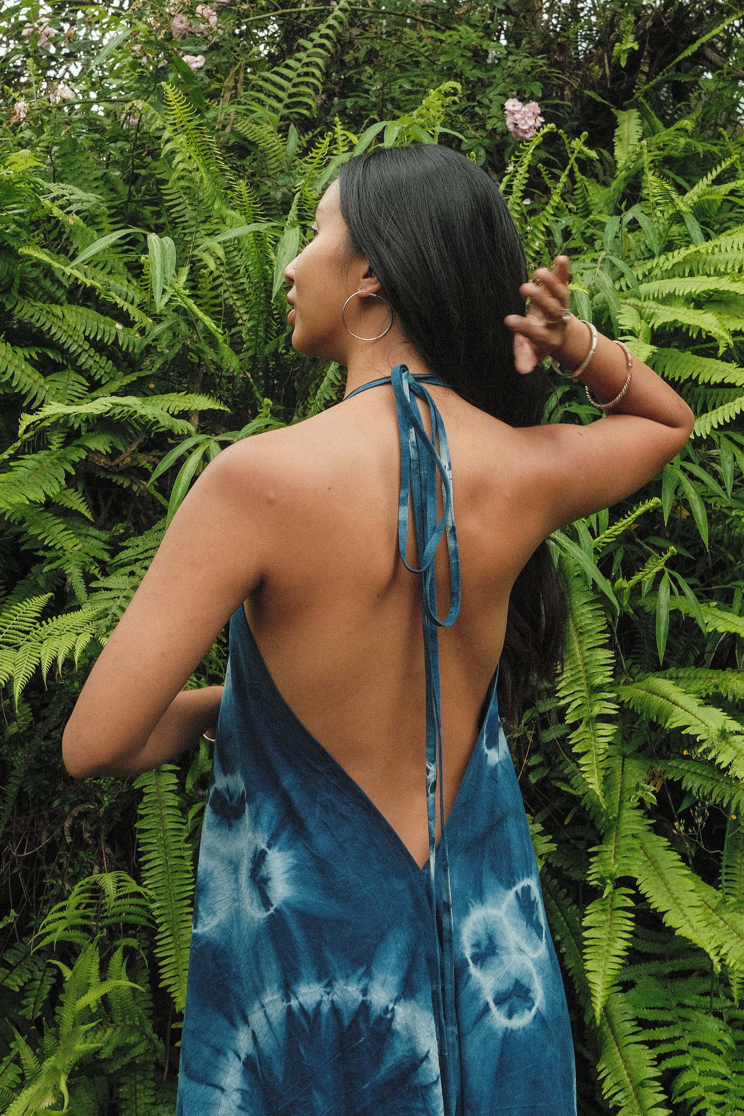 Woman in blue tie-dye backless dress standing in front of lush green ferns.