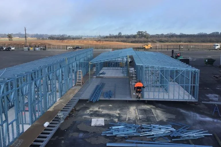 Construction site with steel frame structures being built and a person in an orange vest working.