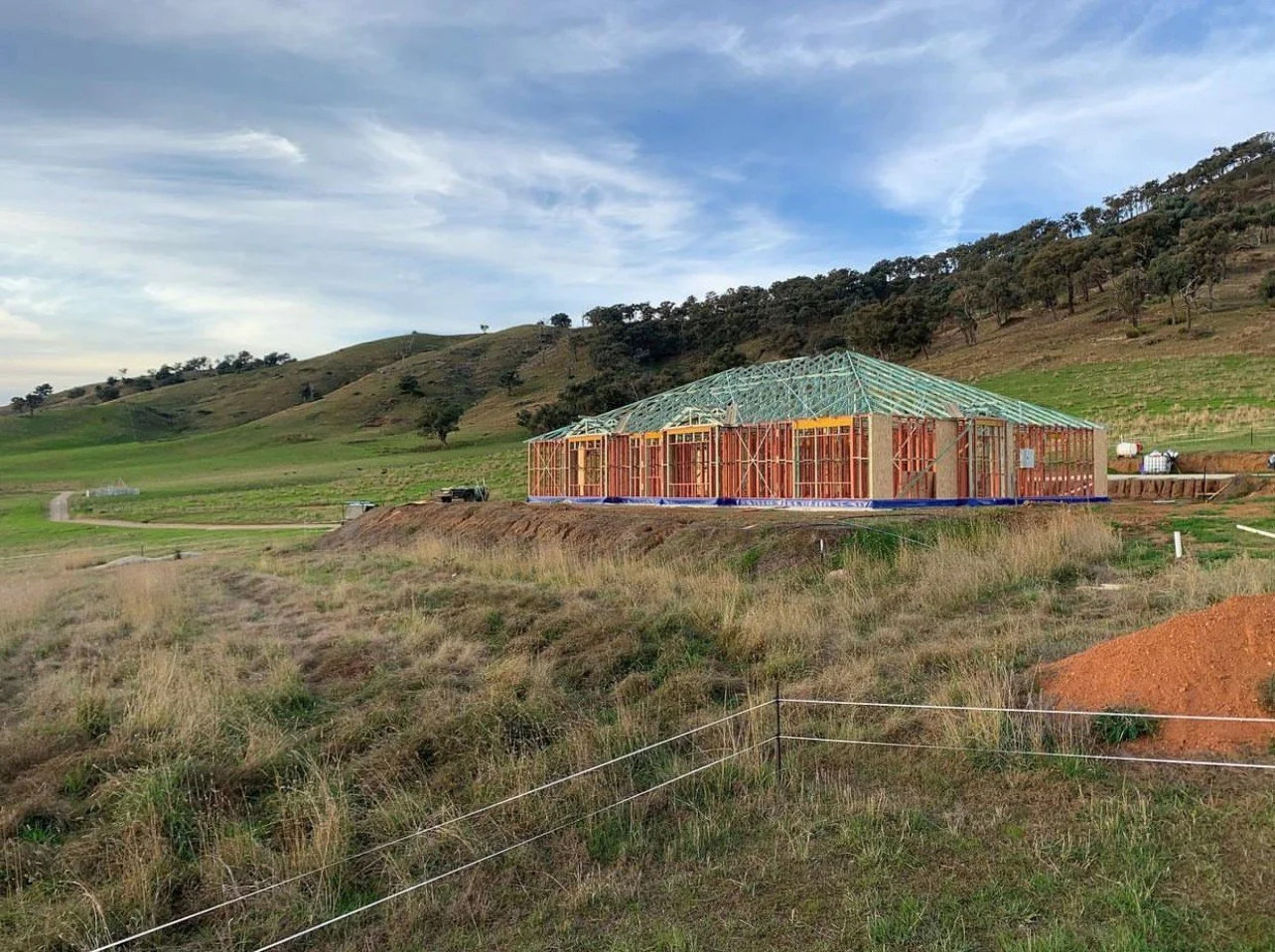 House under construction in rural landscape with hills and trees