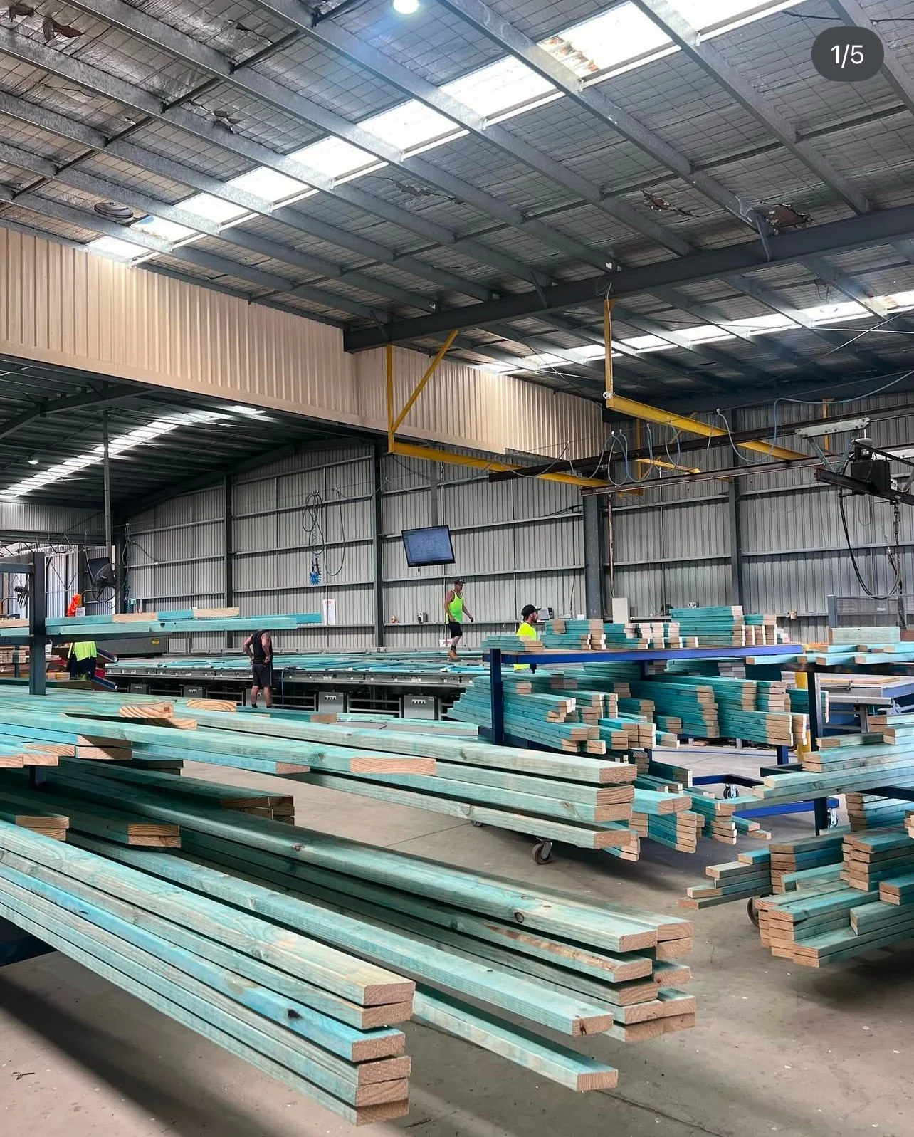 Indoor industrial warehouse with stacks of wooden planks and workers