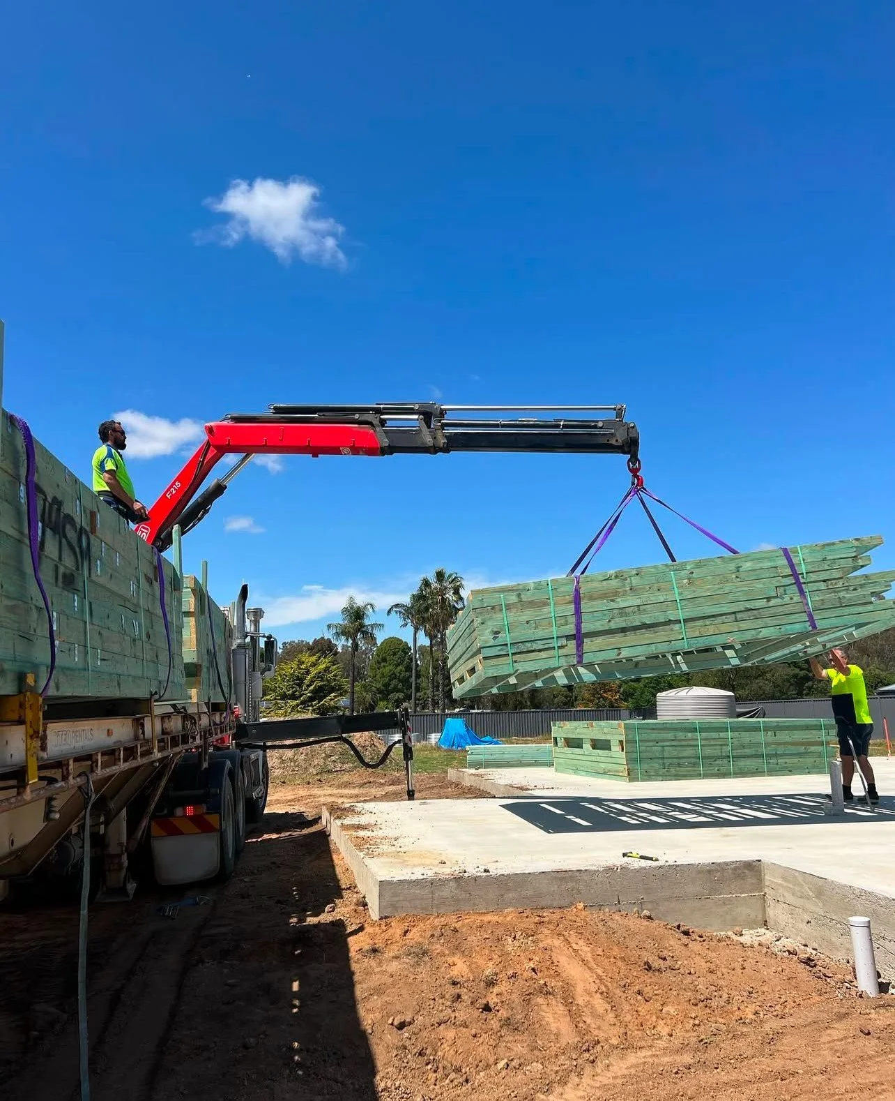Construction site with unloading of wooden beams using a crane on a truck.