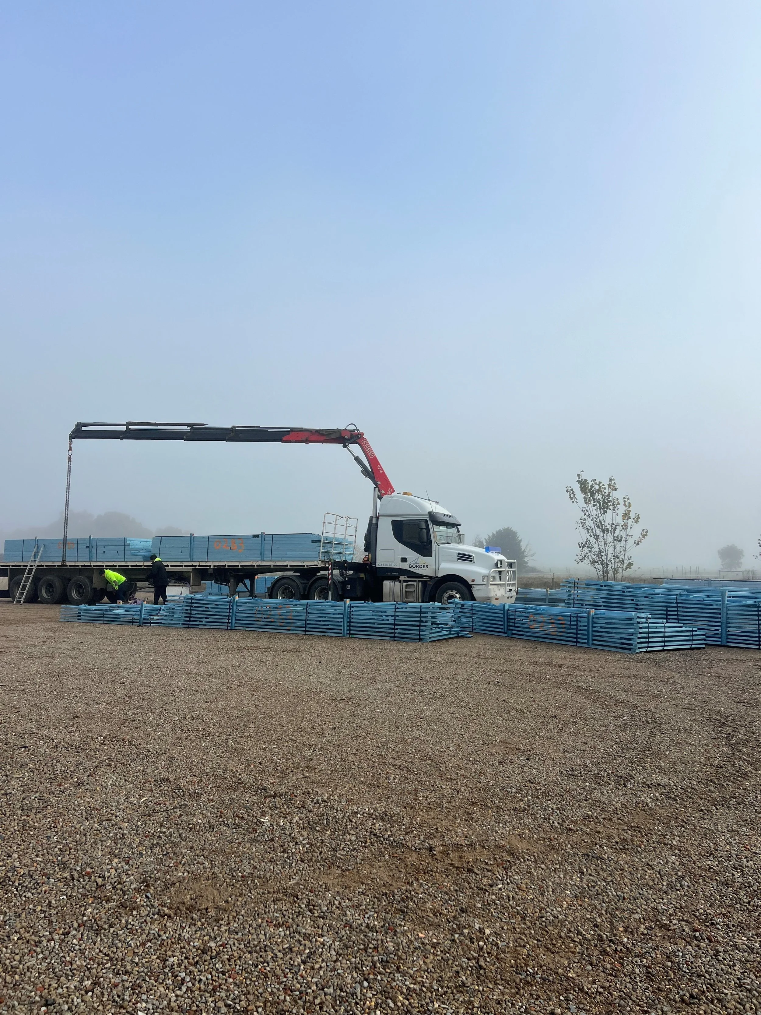 Construction site with truck unloading blue metal beams using a crane arm