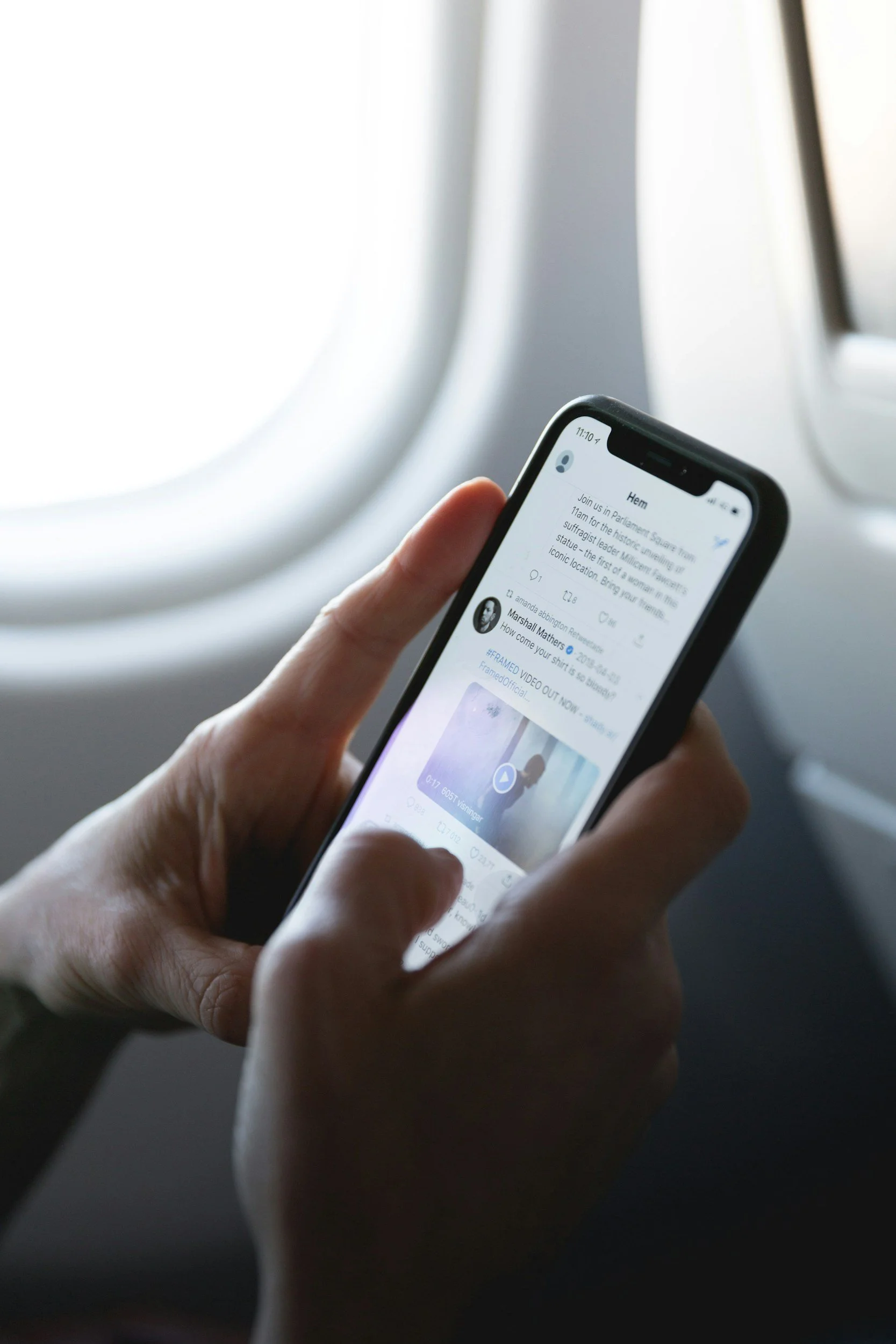 Hands holding a smartphone displaying a social media post in an airplane window seat.