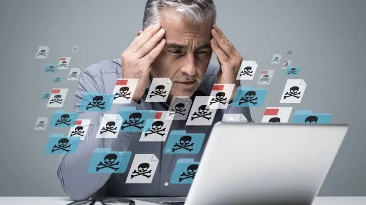 Man looking stressed at laptop with digital folders displaying skull and crossbones symbolizing computer viruses or cyber threats.
