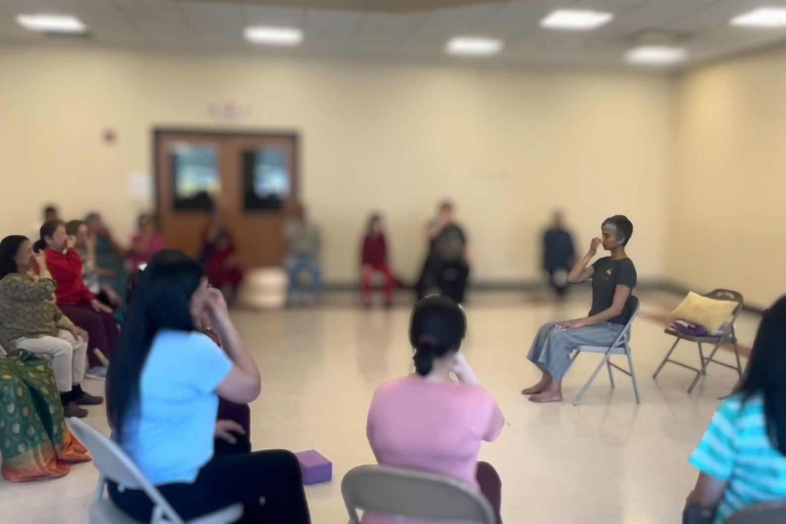 A group of people seated in a circle in a room, with one person sitting on a chair and the others listening.