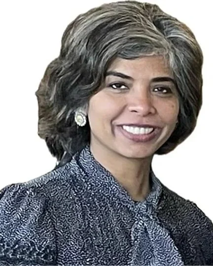 Portrait of a woman with shoulder-length gray hair, wearing earrings and a patterned blue blouse, smiling at the camera.