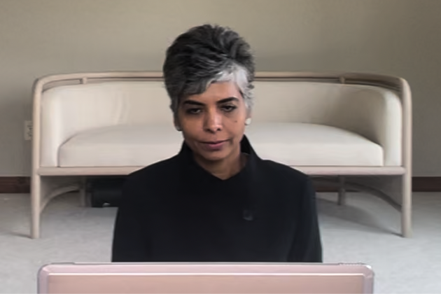 Woman with short gray and black hair looking at a laptop in a room with a white couch in the background.