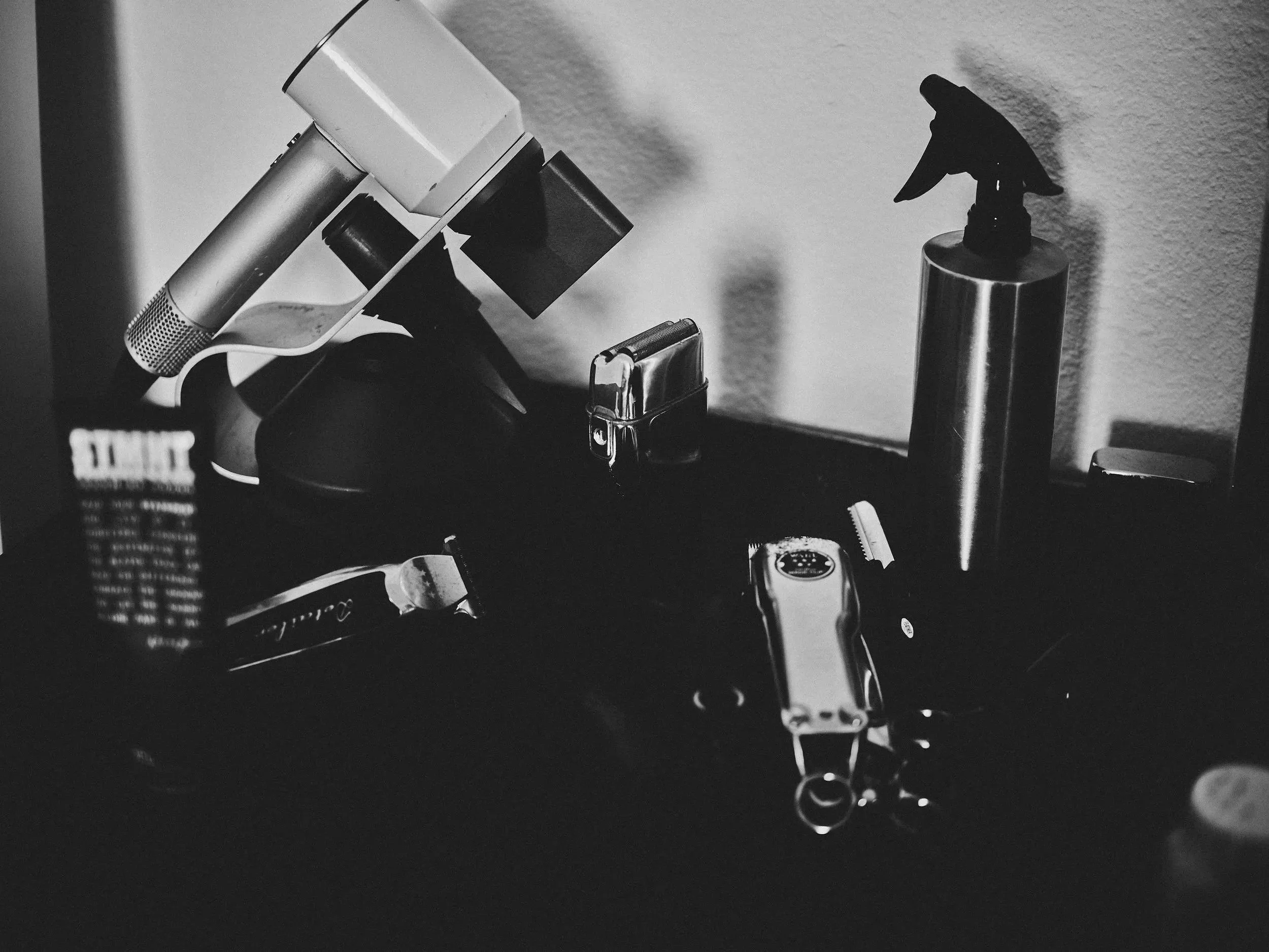 Black and white photo of a collection of personal items on a desk, including a spray bottle, a lighter, a camera, and electronic devices.