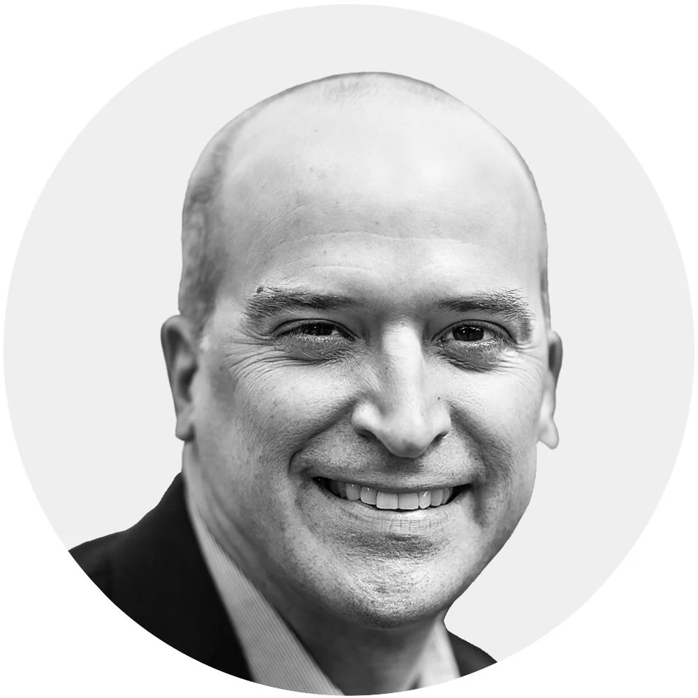 Black and white close-up portrait of a smiling man with a bald head and wearing a suit and white shirt.