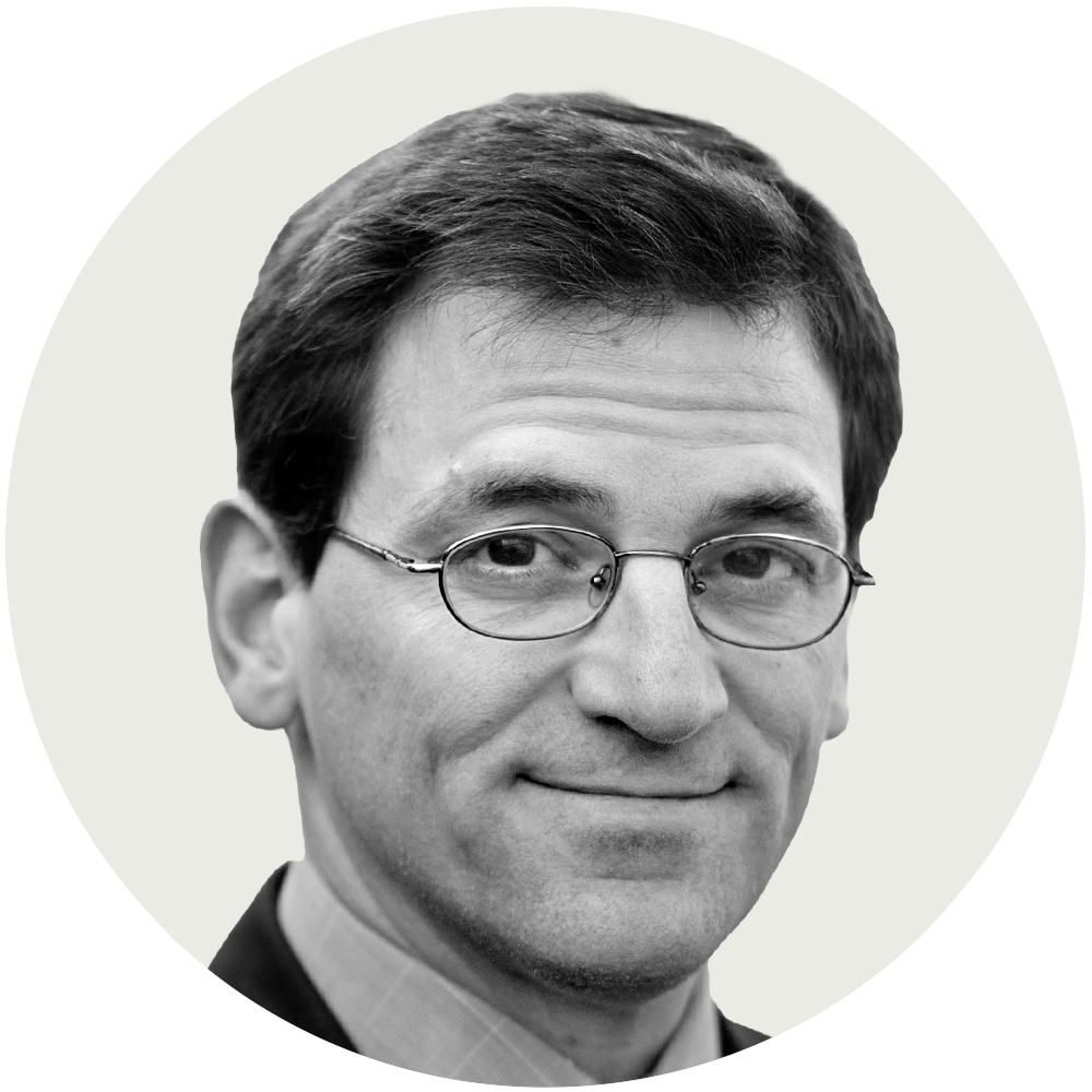 Black and white headshot of a man with short dark hair, wearing glasses and a suit, smiling slightly.